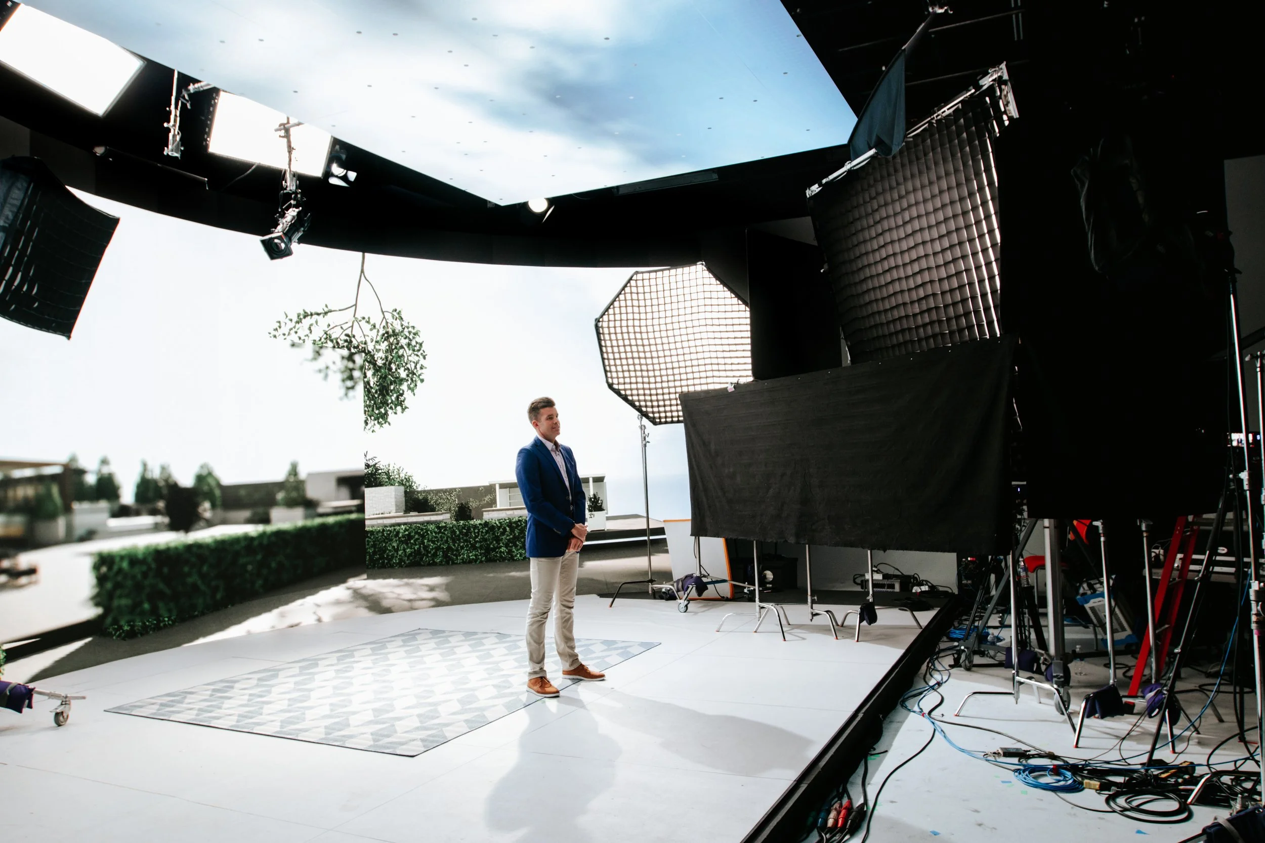 Actor standing on Golden Hour’s LED volume stage with a virtual environment displayed on the screen behind him, along with partial view of off-stage production equipment.