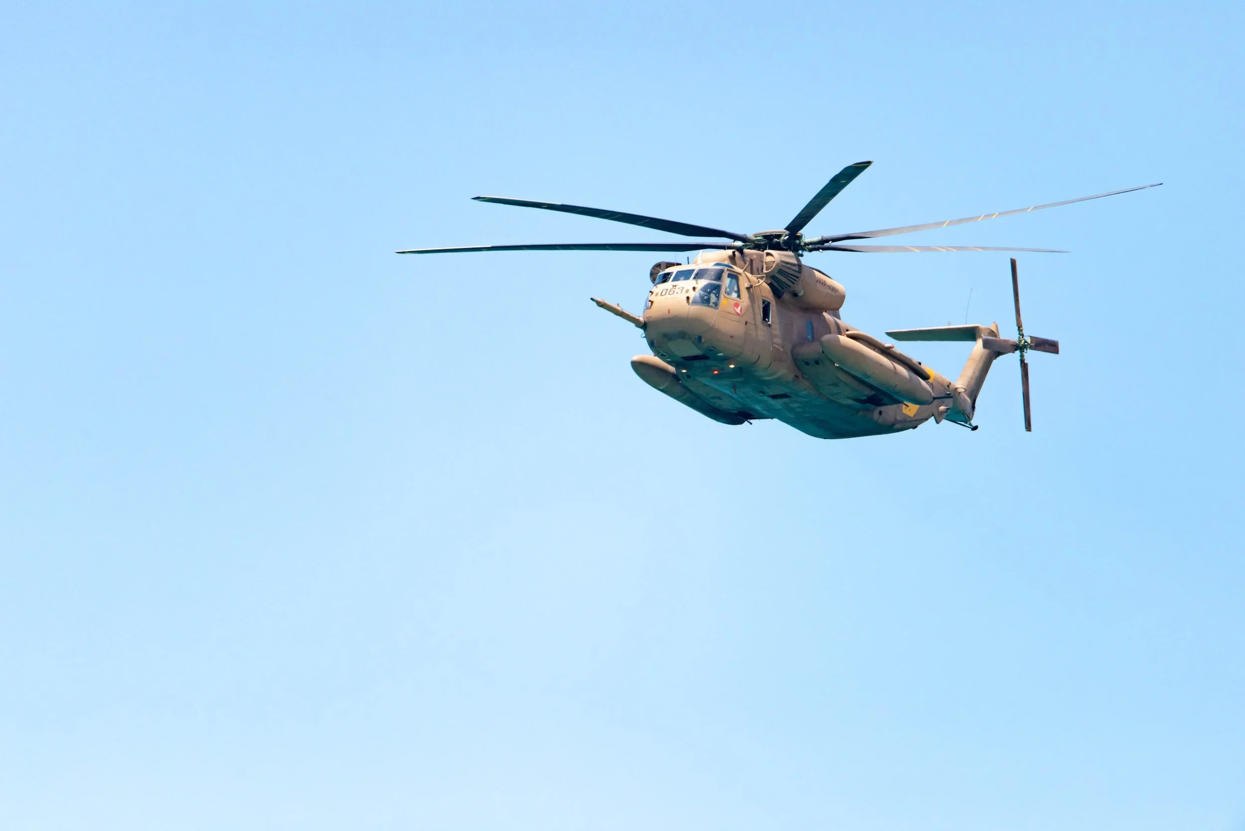 A military helicopter flying in clear blue sky.
