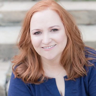 Smiling woman with red hair wearing a blue top seated outdoors