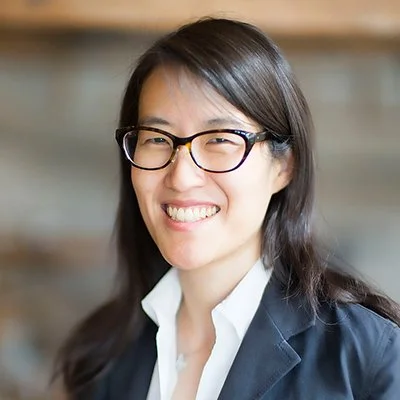 Person wearing glasses and a suit, smiling, with a blurred background.