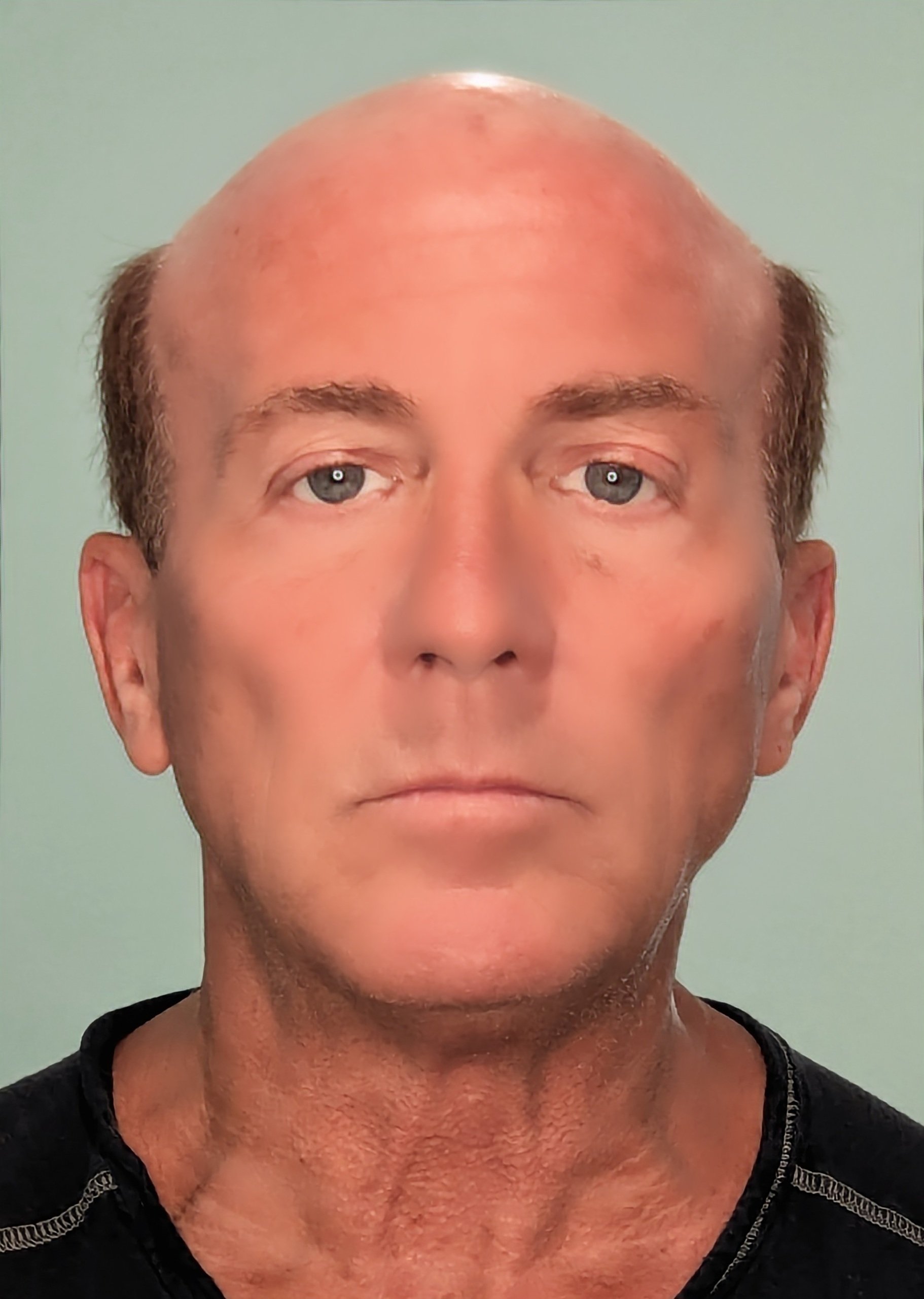 A close-up portrait of an older man with a bald head, blue eyes, and fair skin, wearing a black shirt against a light green background.