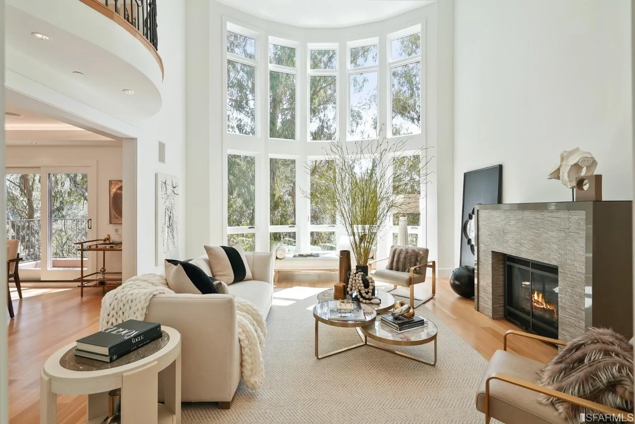 Open-concept living room remodel with double-height windows, wide-plank hardwood floors, a modern fireplace surround, and abundant natural light—San Francisco Bay Area general contractor, Pinnacle Construction.