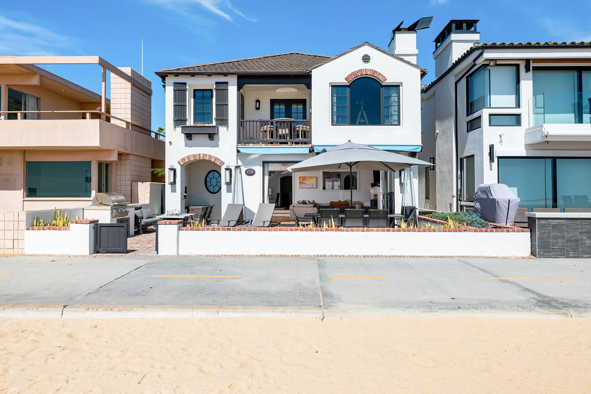 A row of modern houses with outdoor patios, umbrellas, and lounge chairs, under a bright blue sky.