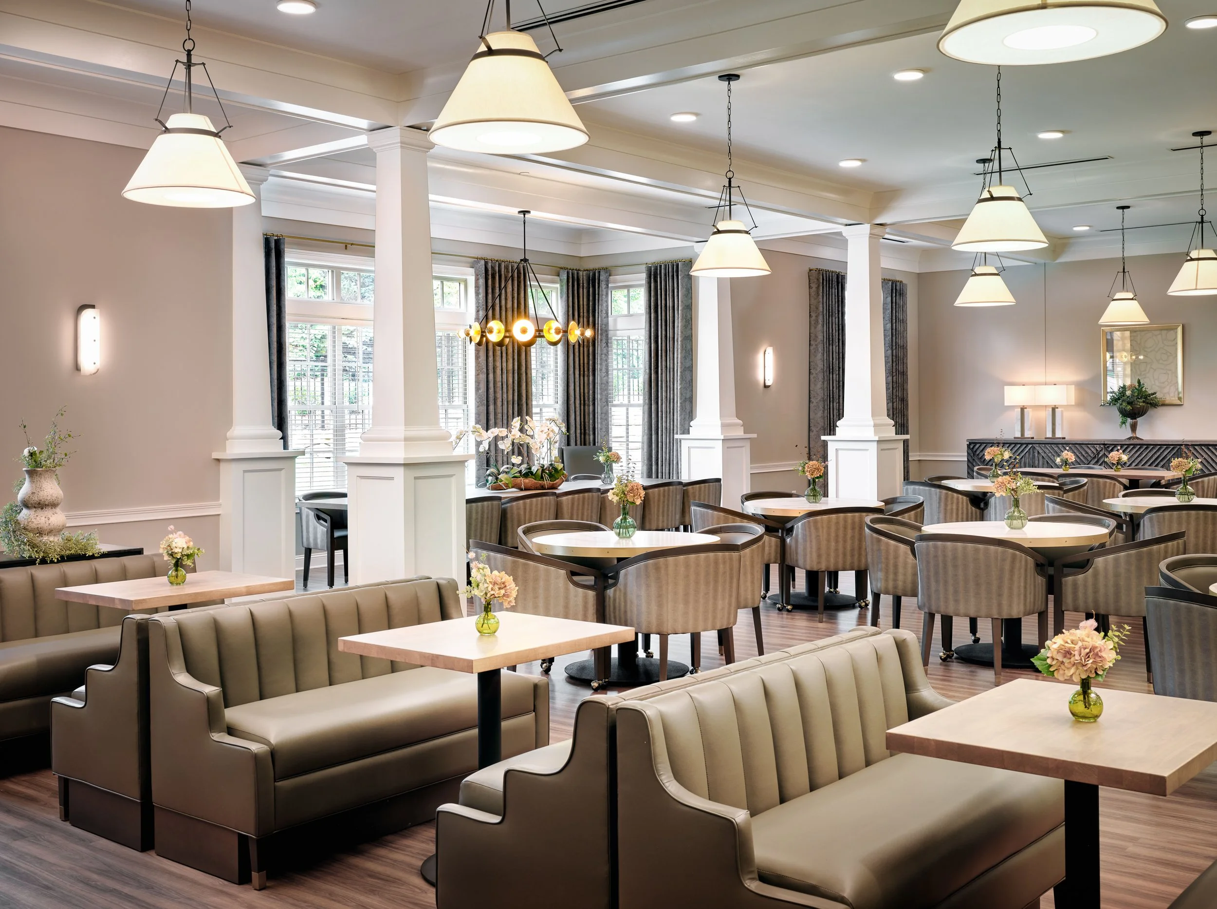 Thistle & Oak dining room with taupe leather banquettes, barrel chairs, marble-topped tables, oversized cone pendants, and floral centerpieces, designed by Ashley Schneider