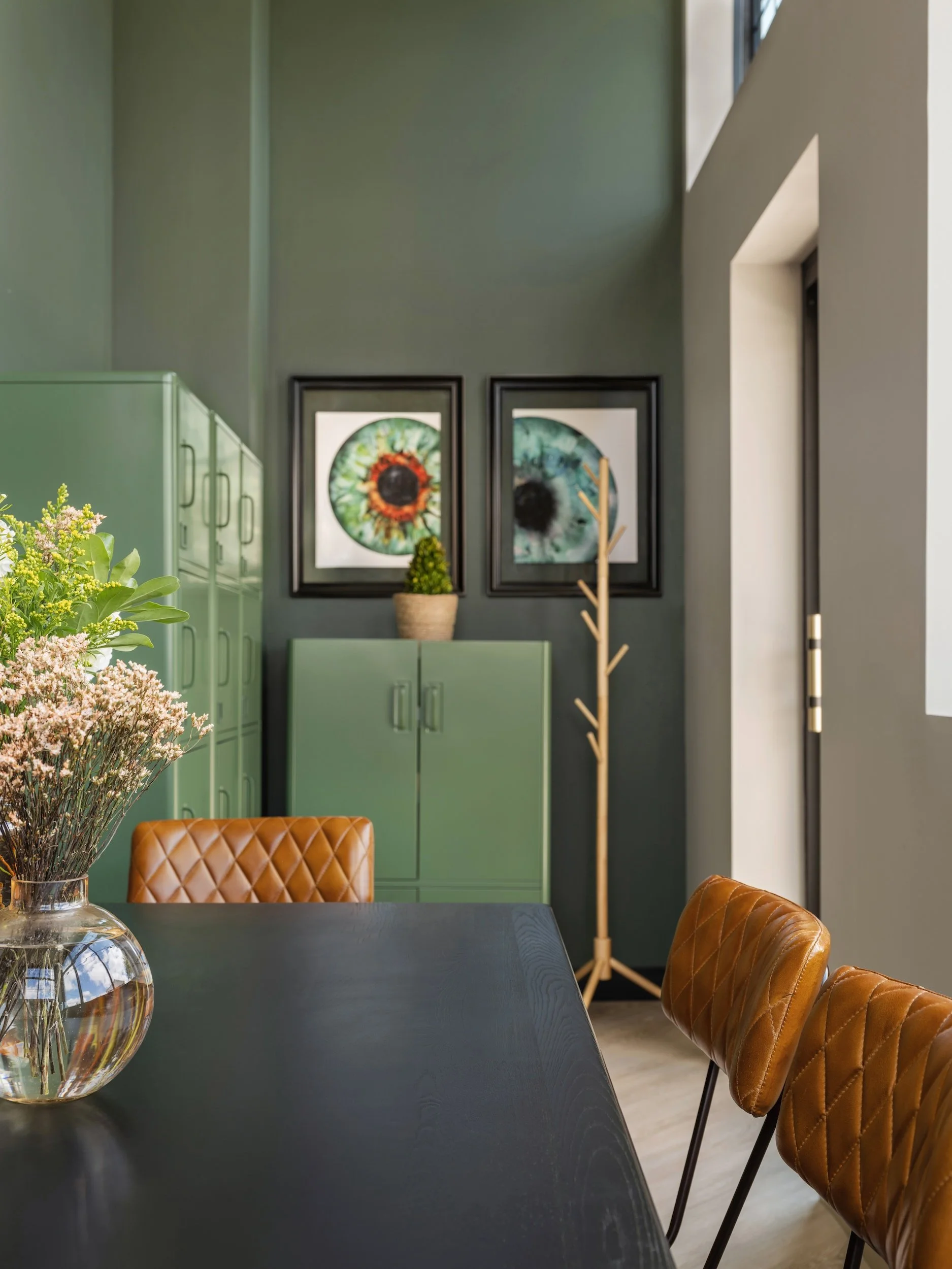 Sage green staff locker wall with eye anatomy artwork, a black table, and cognac leather chairs, designed by Luxe Style Studio