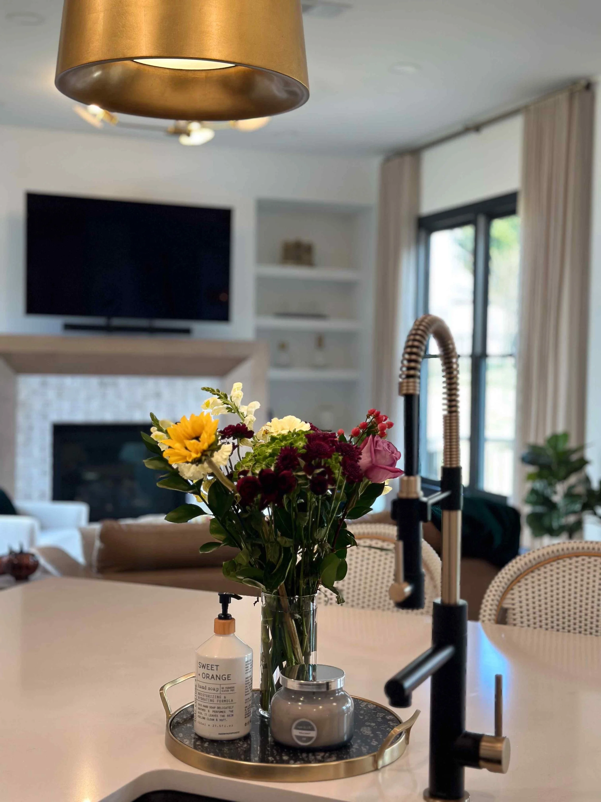 Styled kitchen island with black gooseneck faucet and gold drum pendant lights overlooking open-concept living area, Luxe Style Studio