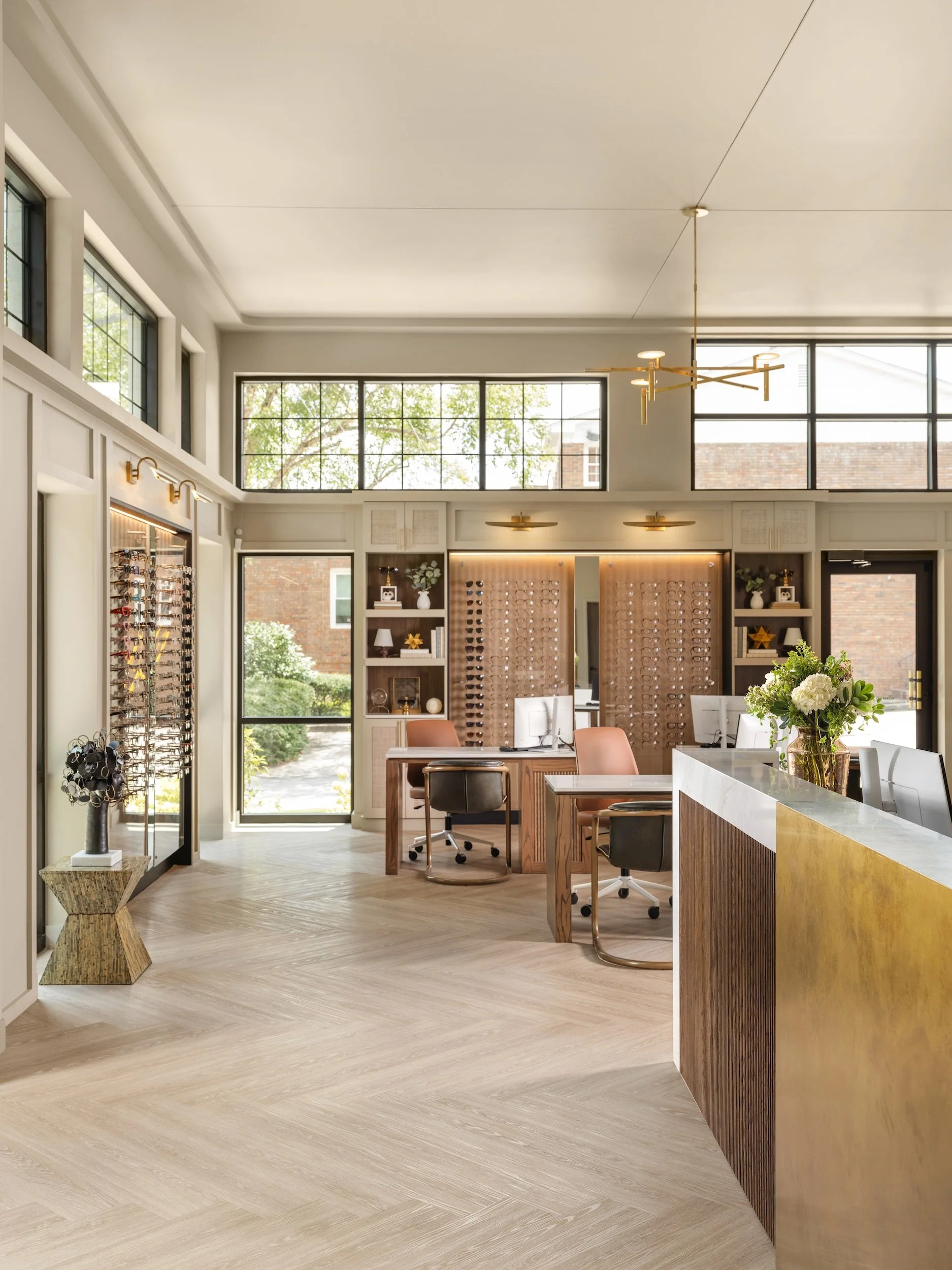 Windsor Eye Care interior with a custom reception desk, illuminated eyewear displays, brass lighting, and herringbone floors, designed by Luxe Style Studio