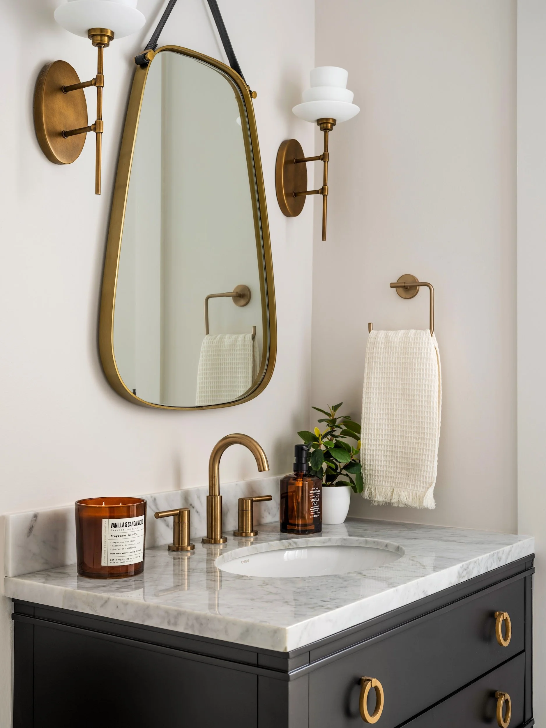 Powder room with matte black vanity, white marble countertop, brass ring hardware, leather strap brass-framed mirror, and globe brass sconces, Atlanta, GA private residence, interior design by Luxe Style Studio