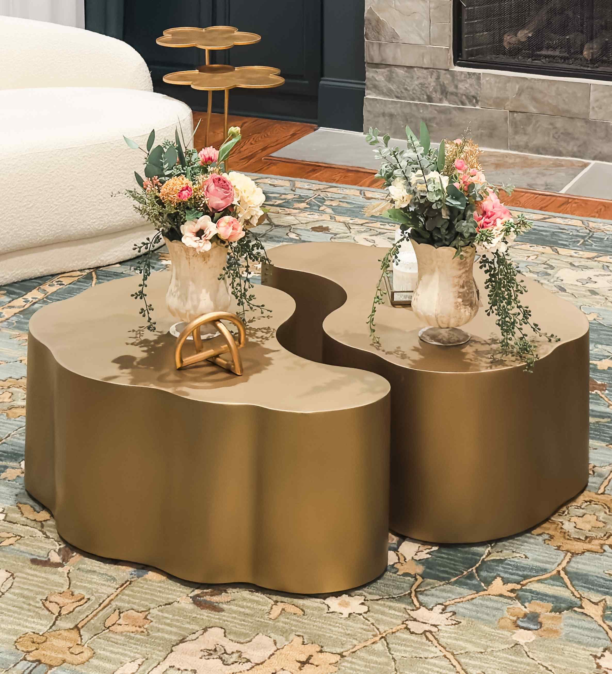 East Cobb living room with sculptural gold cloud-form nesting coffee tables, cream bouclé sofa, and blue floral rug beside stone fireplace, East Cobb, GA private residence, interior design by Luxe Style Studio