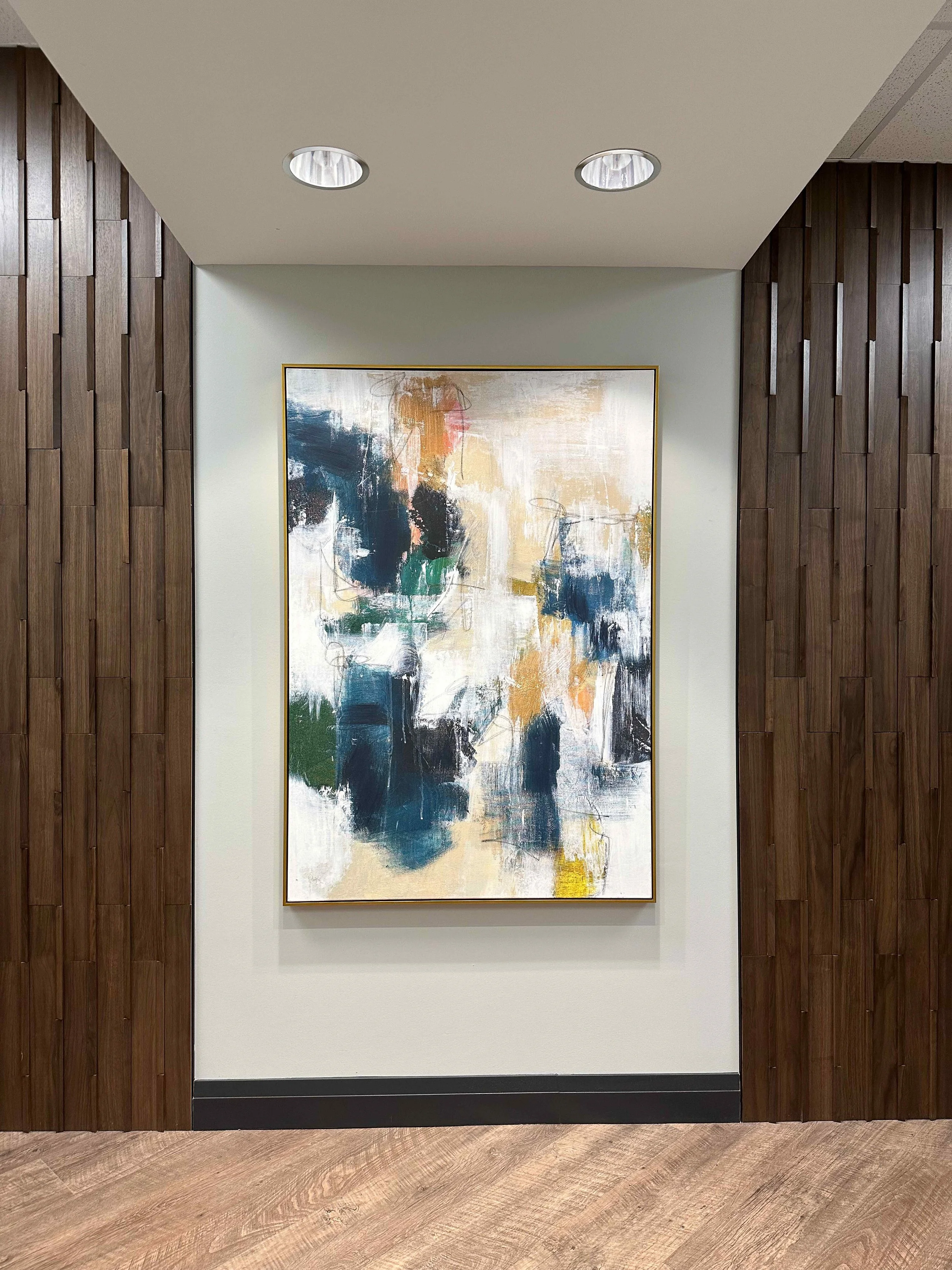 Large-scale abstract painting in gold frame displayed in recessed niche between floor-to-ceiling walnut wood slat accent walls in corporate office hallway, interior design by Luxe Style Studio
