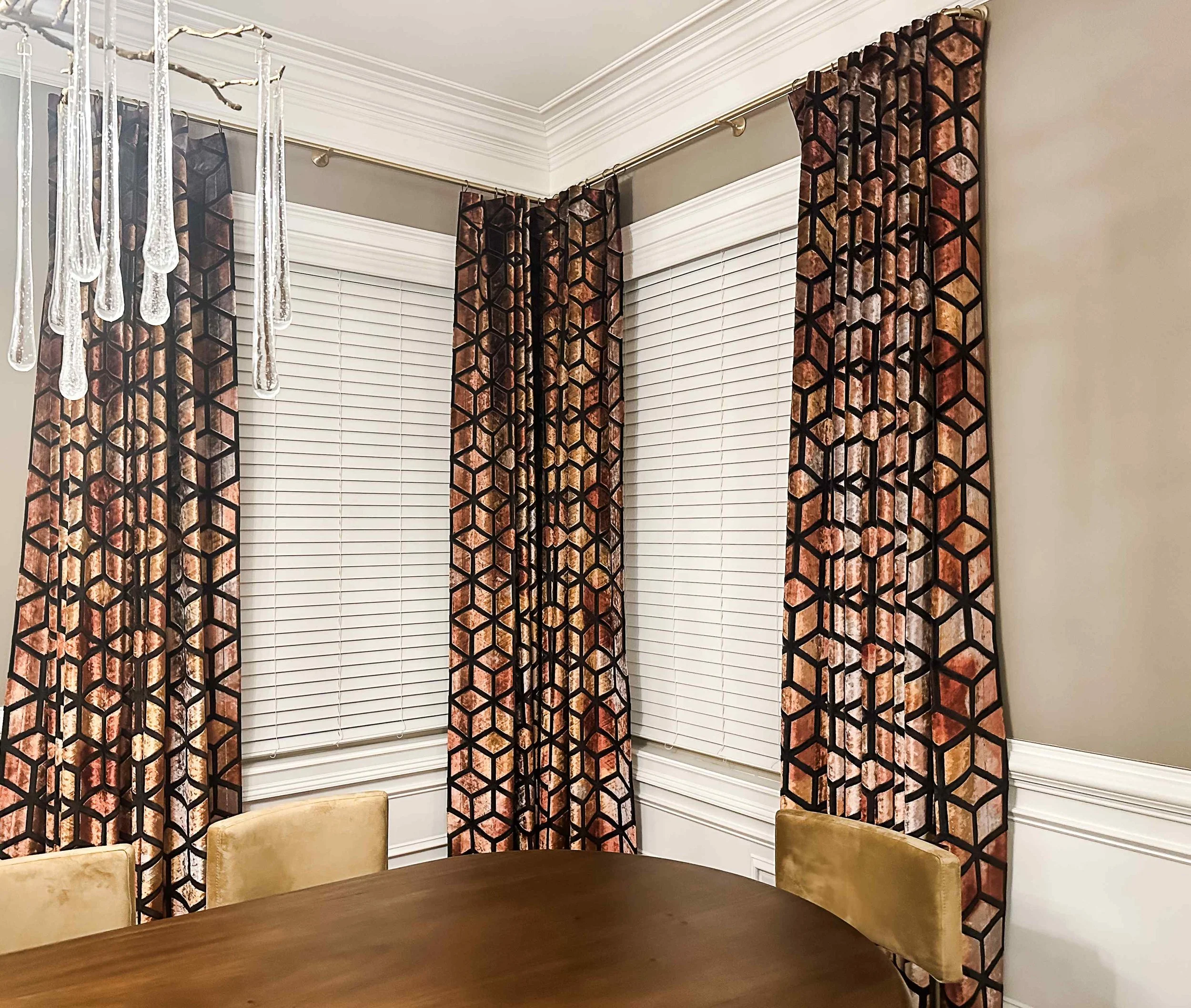 Noble dining-room bay window with geometric copper velvet drapery and a brass crystal chandelier, designed by Luxe Style Studio