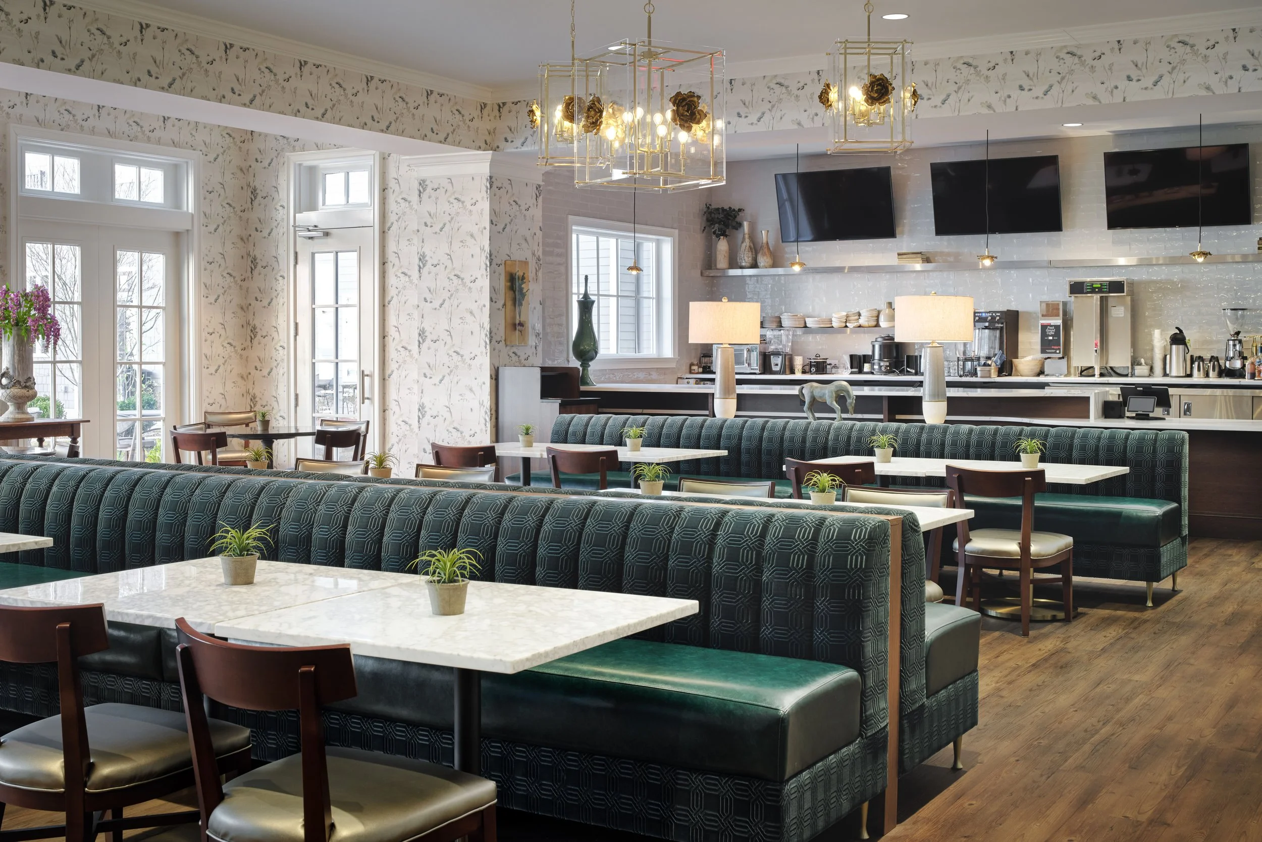 Zinnia Café & Market dining room with tufted green velvet booths, white marble tables, and brass geometric chandeliers, designed by Ashley Schneider