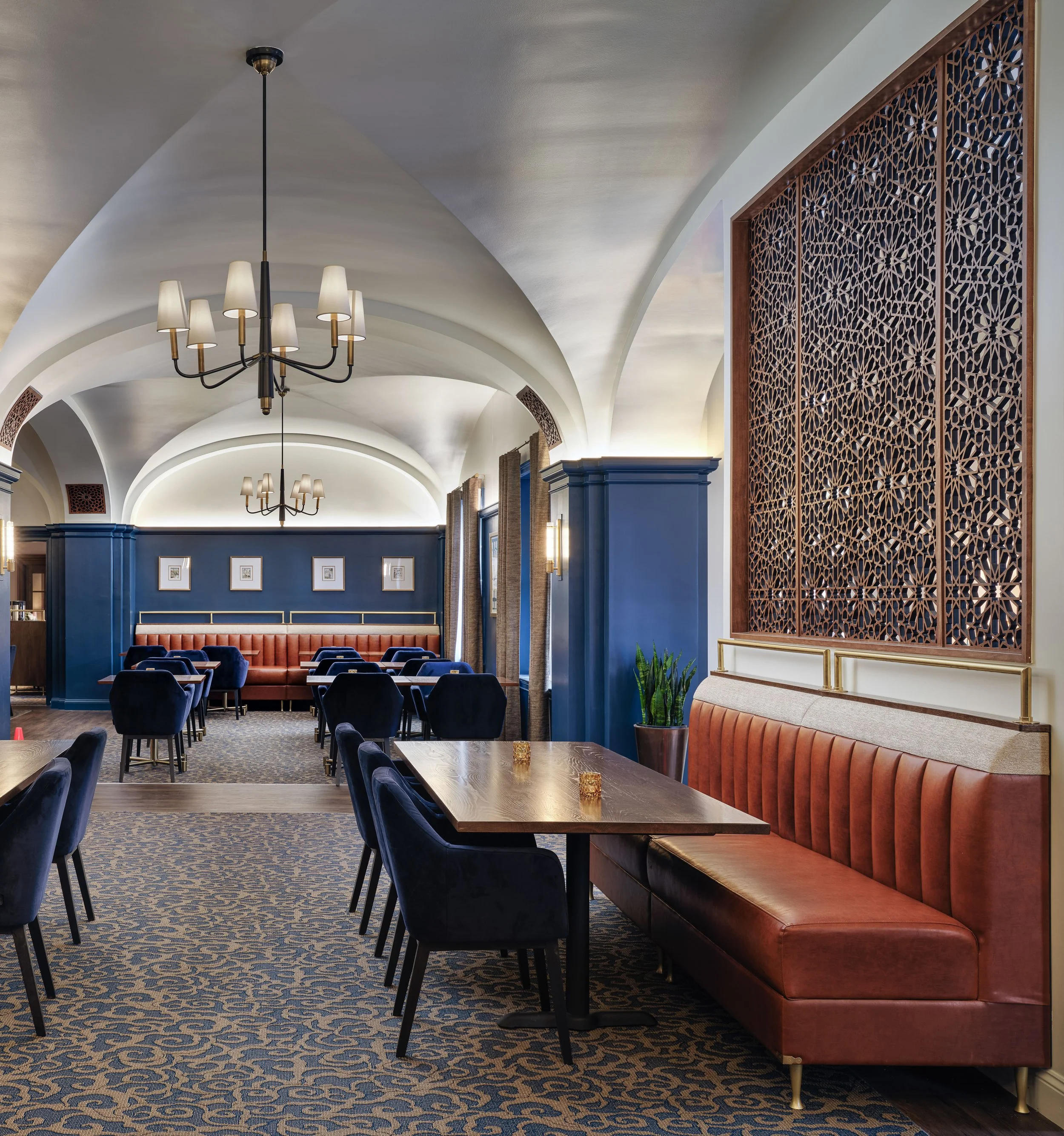 Off The Rails dining room with groin-vaulted ceilings, navy walls, cognac leather banquettes, velvet chairs, and carved lattice screens, designed by Ashley Schneider