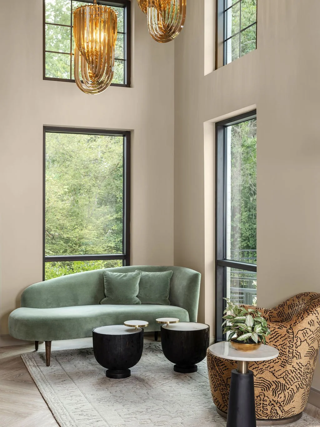 Luxury commercial waiting room with curved sage green velvet sofa, amber glass chandelier, black sculptural coffee tables, and floor-to-ceiling black steel windows, interior design by Luxe Style Studio