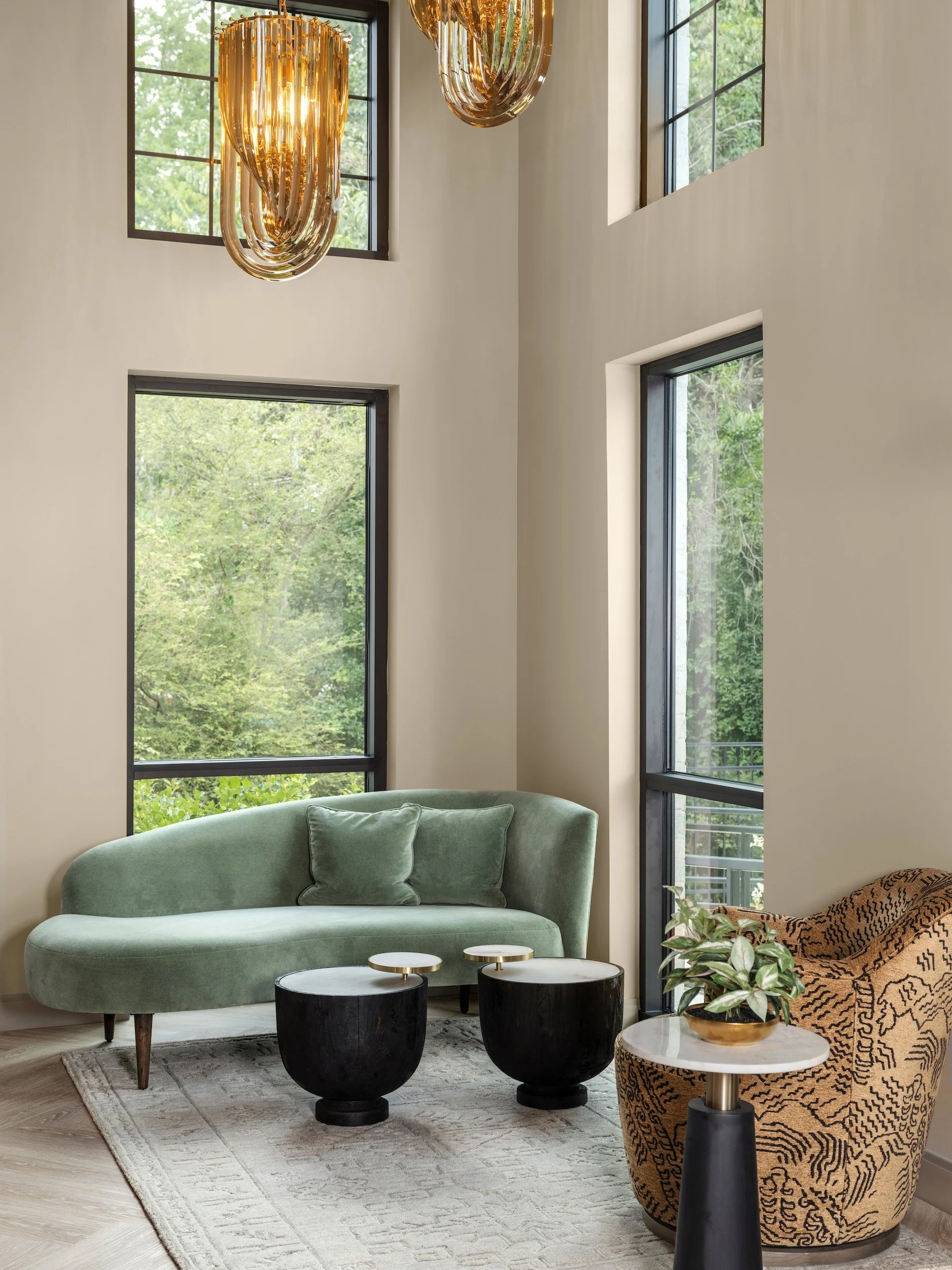 Luxury commercial waiting room with curved sage green velvet sofa, amber glass chandelier, black sculptural coffee tables, and floor-to-ceiling black steel windows, Windsor Eye Care optical boutique, Atlanta, GA, interior design by Luxe Style Studio