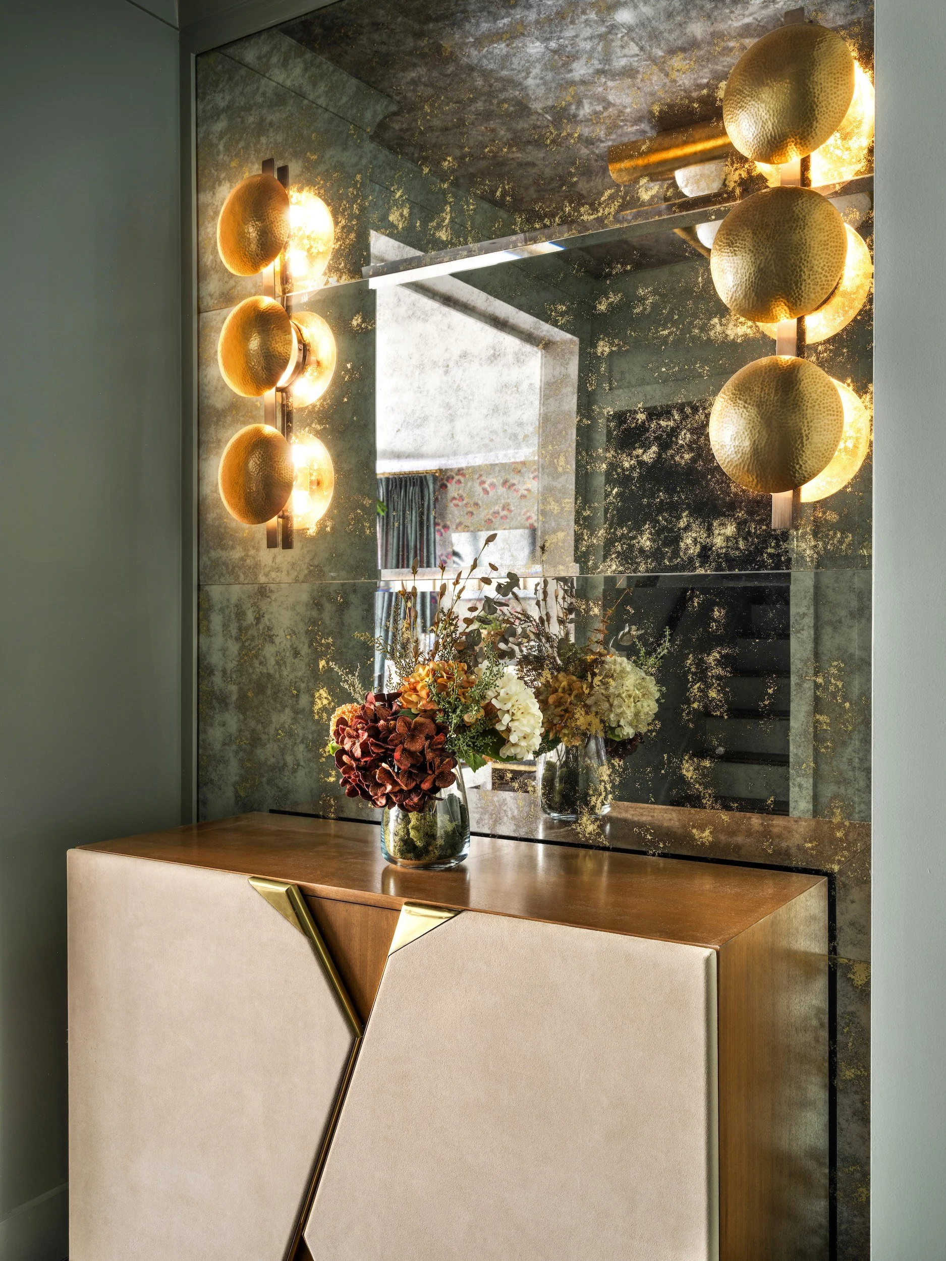 Antiqued mirror wall with hammered brass sconces and a leather-and-brass console, designed by Luxe Style Studio