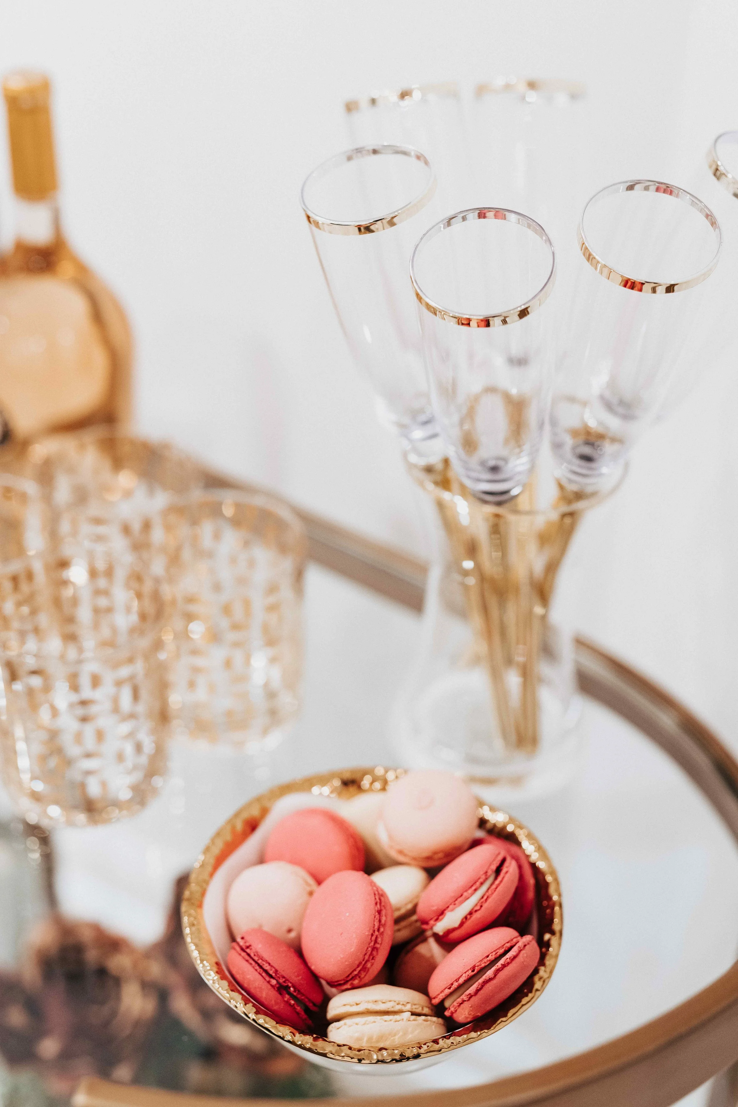 Luxury medical spa hospitality detail with French macarons in gold bowl, crystal champagne flutes, and cut crystal glasses on mirrored tray, interior design by Luxe Style Studio