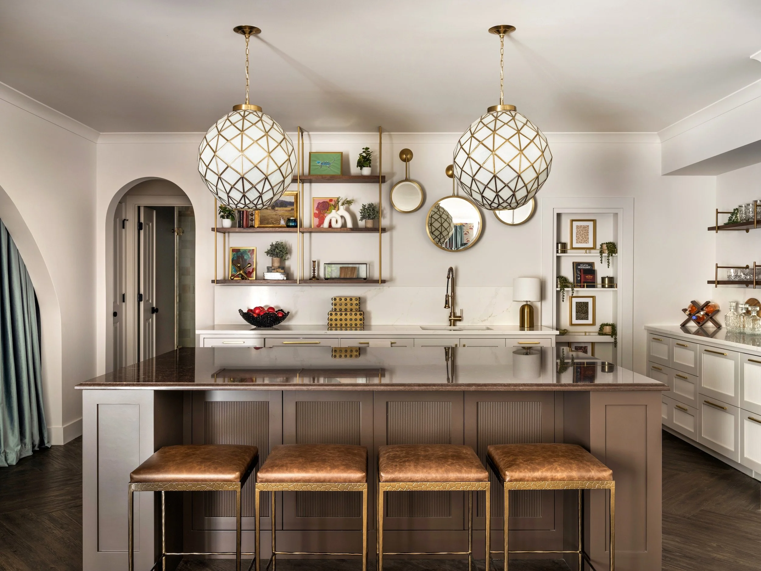 Glamorous living room with gold velvet swivel chairs, sculptural brass and glass coffee table, capiz shell chandelier, and open view to kitchen bar, interior design by Luxe Style Studio