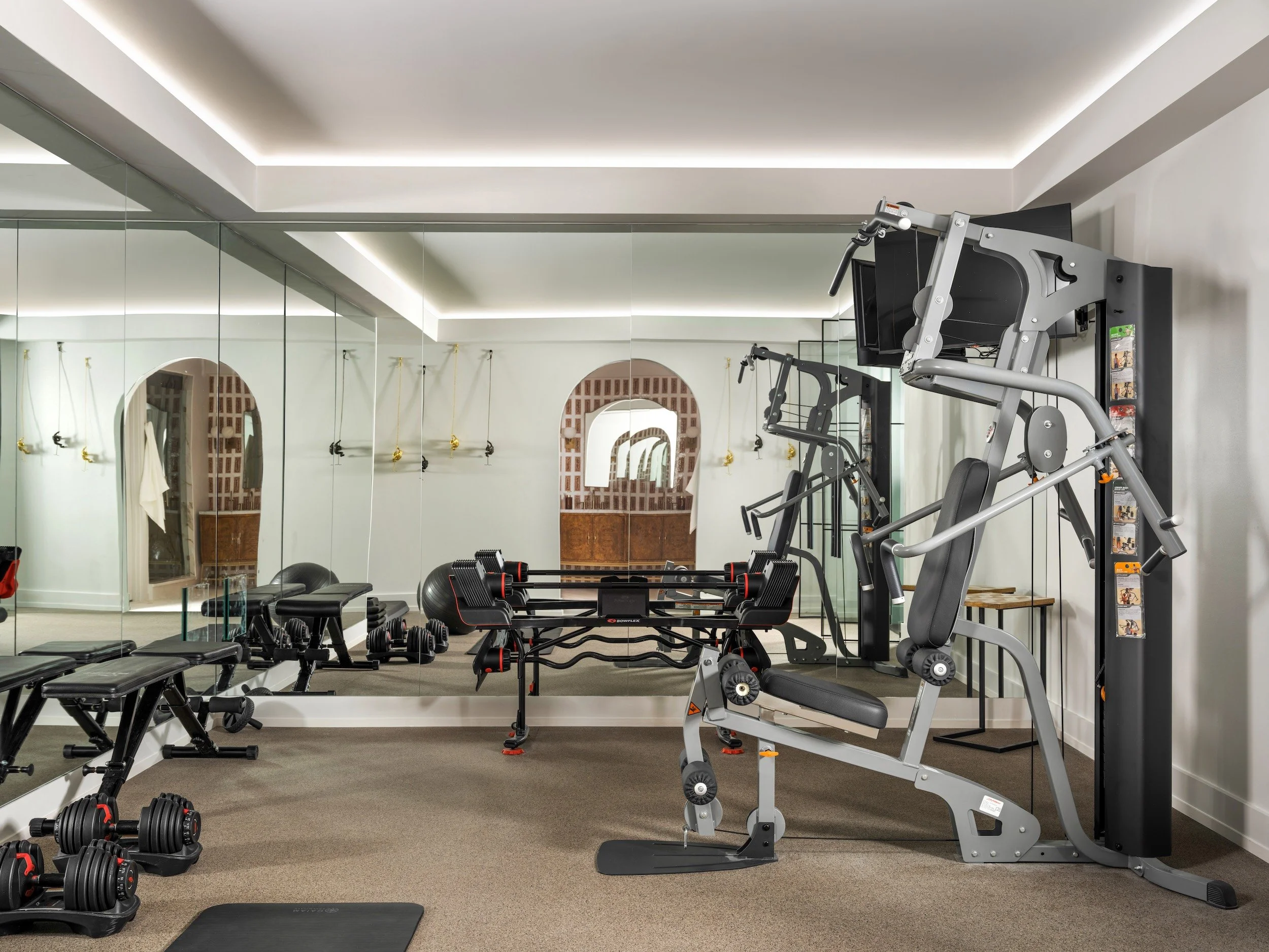 Home gym with mirrored walls, cove lighting, and an arched doorway, designed by Luxe Style Studio