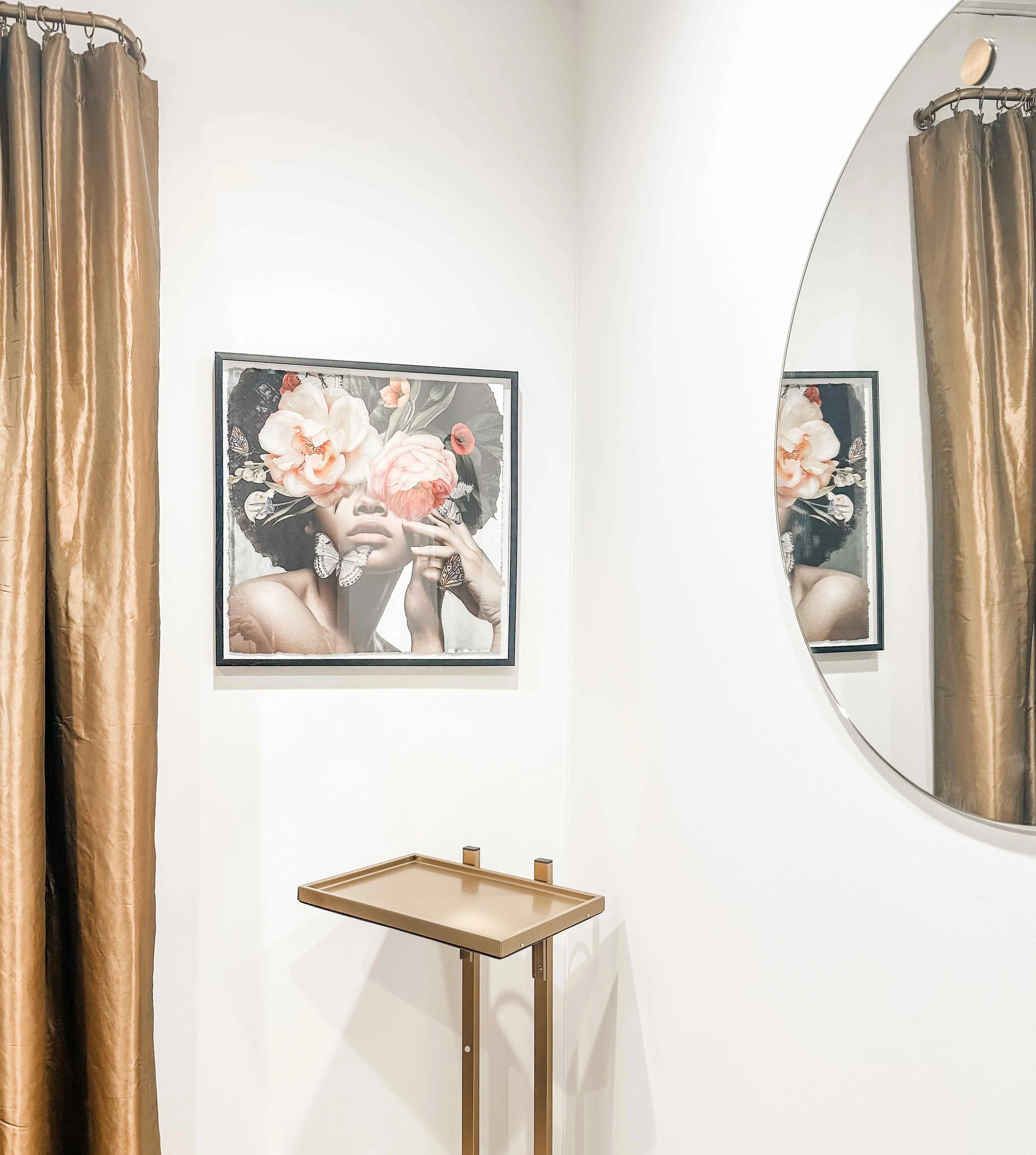 Luxury spa treatment room with floor-to-ceiling gold silk drapes, framed floral portrait artwork, brass treatment tray stand, and large round frameless mirror, interior design by Luxe Style Studio