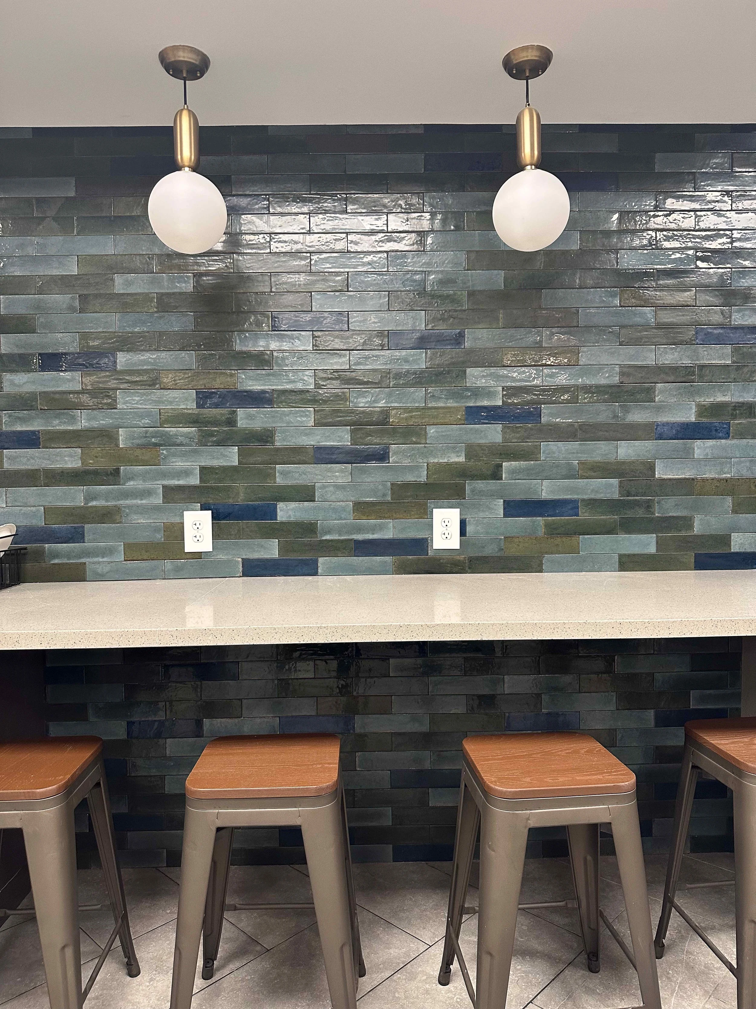 Corporate break room bar counter with multicolor zellige tile full-height accent wall, white quartz countertop, metal and wood bar stools, and brass globe pendant lights, interior design by Luxe Style Studio