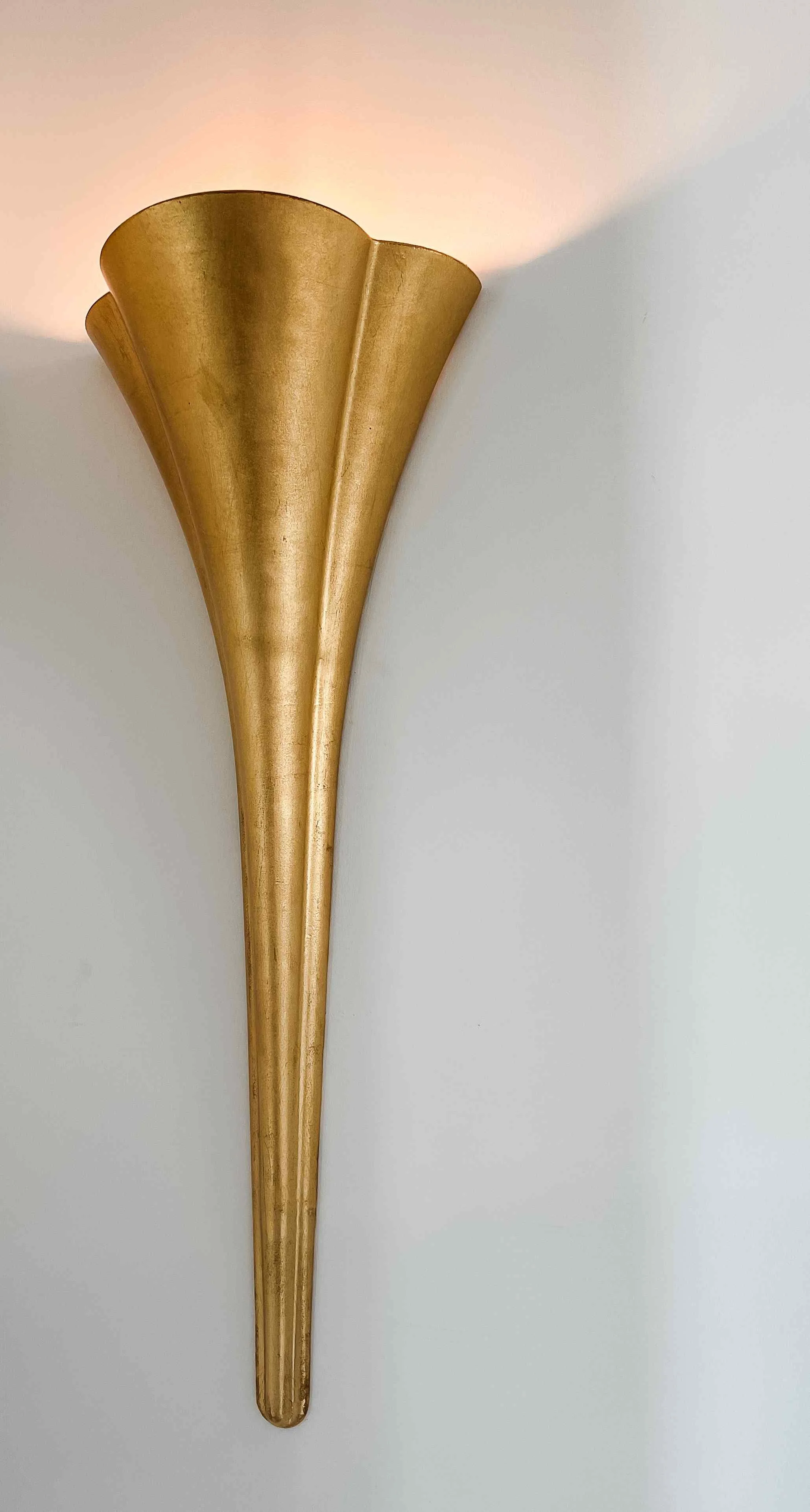 Sculptural gold leaf trumpet wall sconce casting upward ambient light, curated by Luxe Style Studio