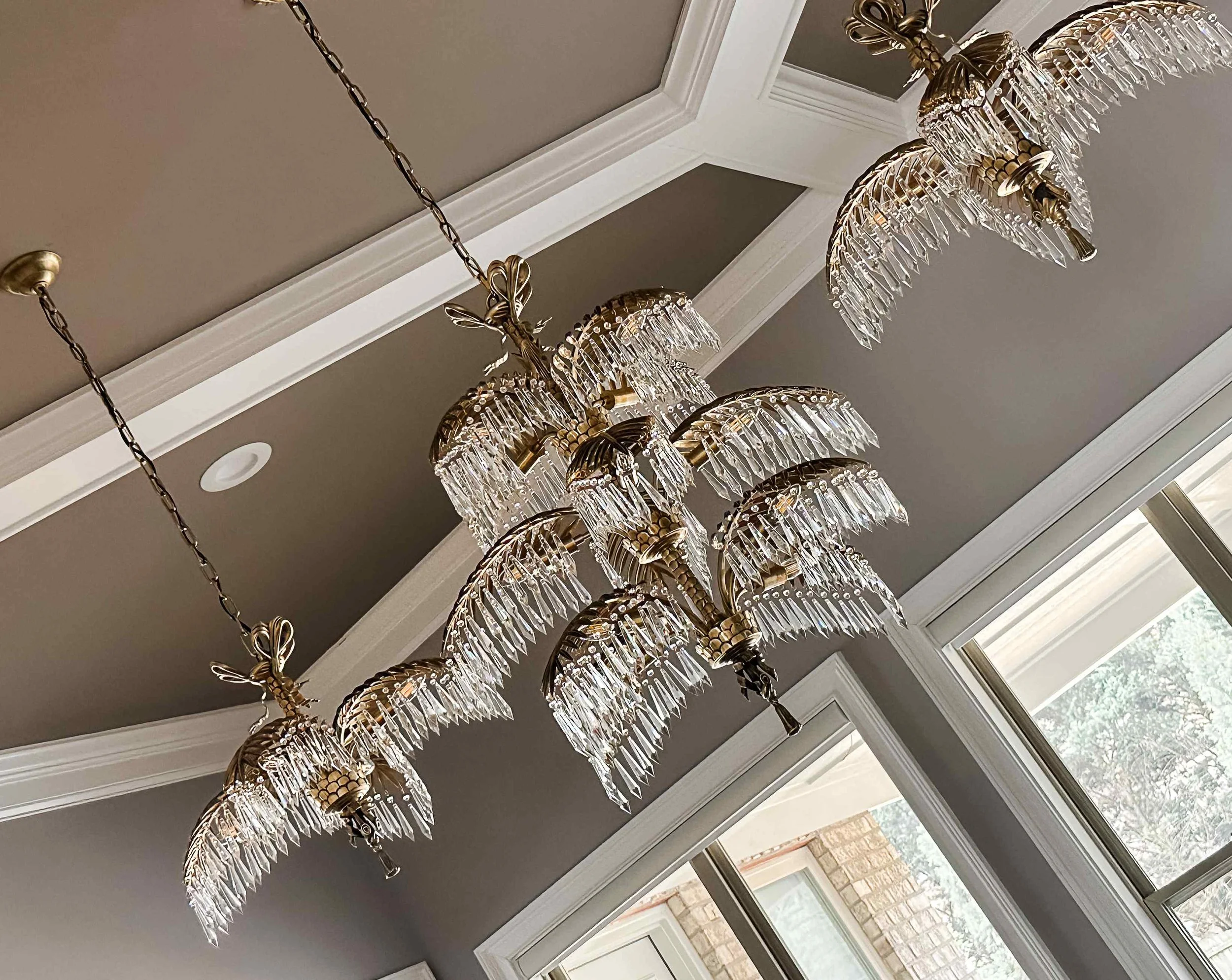 Noble living room in East Cobb with three tiered crystal palm chandeliers suspended beneath a dark coffered ceiling, designed by Luxe Style Studio