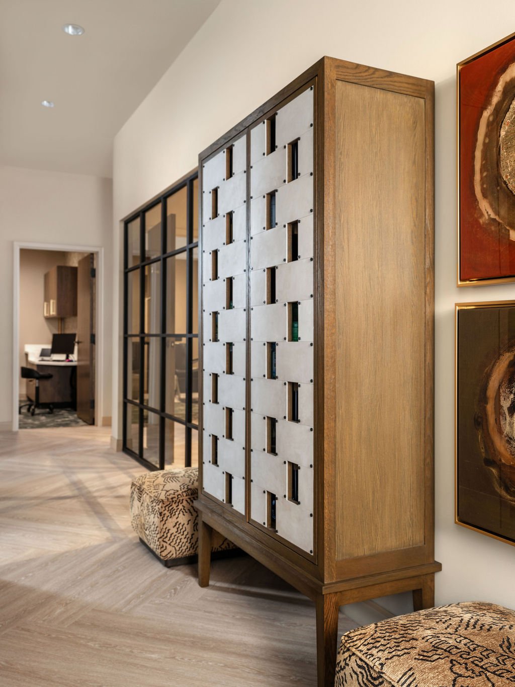 Custom oversized woven leather and oak cabinet used as room divider in luxury commercial interior with herringbone floors and abstract art, interior design by Luxe Style Studio