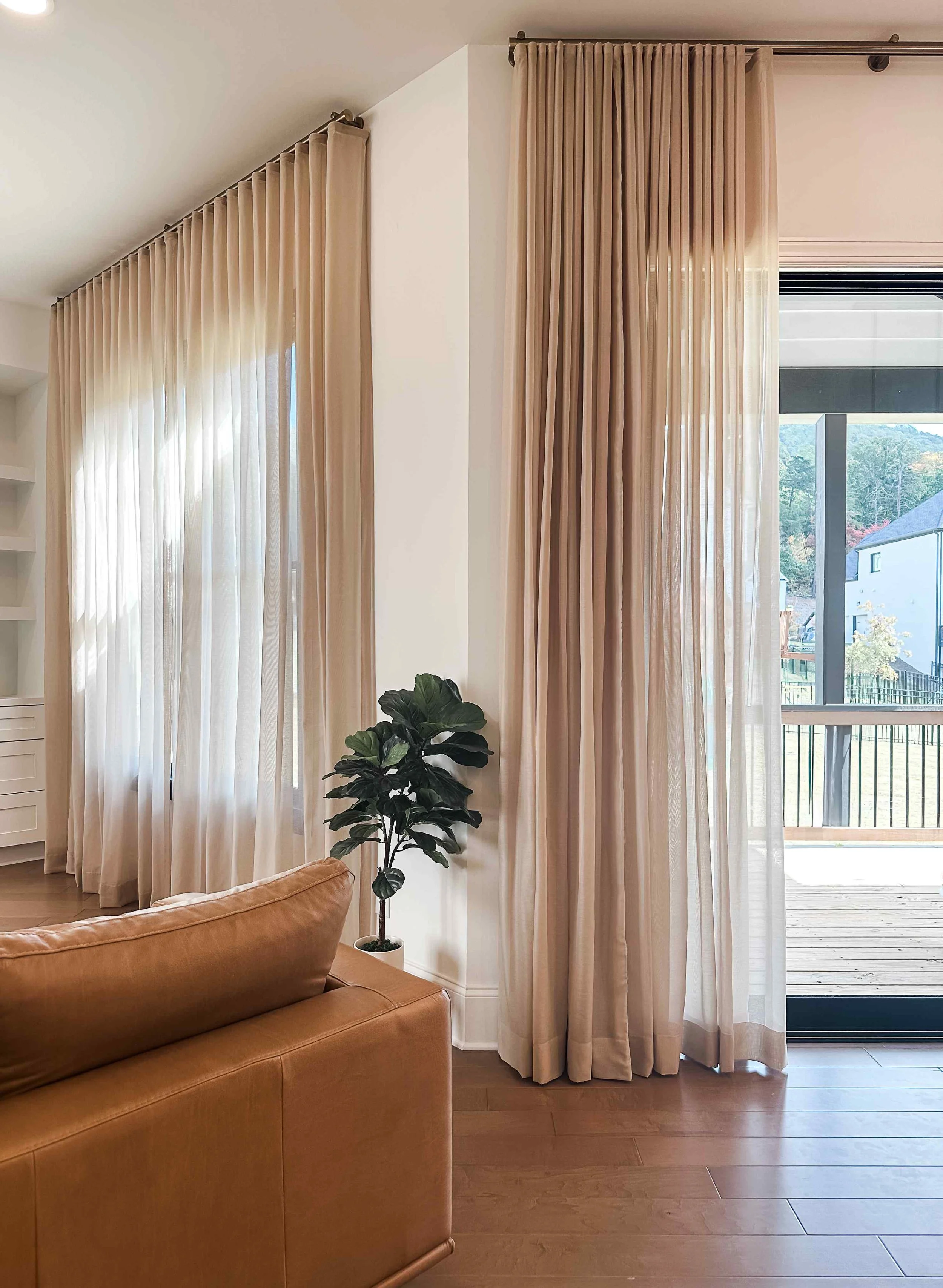 Ripple fold neutral linen curtains framing sliding glass door with leather sofa, designed by Luxe Style Studio