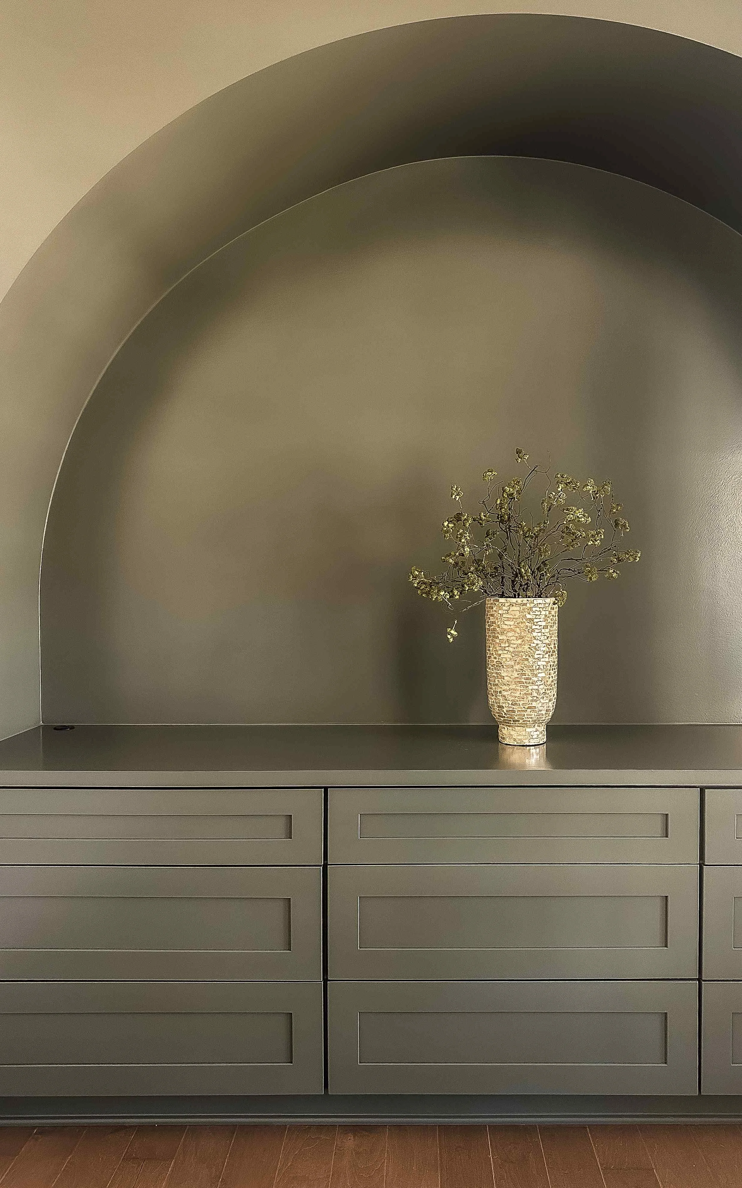Dramatic olive green arched wall niche with matching built-in cabinetry and sculptural vase styling by Luxe Style Studio