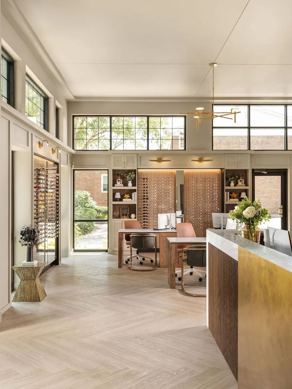 Luxury optical boutique interior with wall-mounted eyewear displays, herringbone white oak floors, brass pendant lighting, and floor-to-ceiling steel windows, Atlanta, interior design by Luxe Style Studio