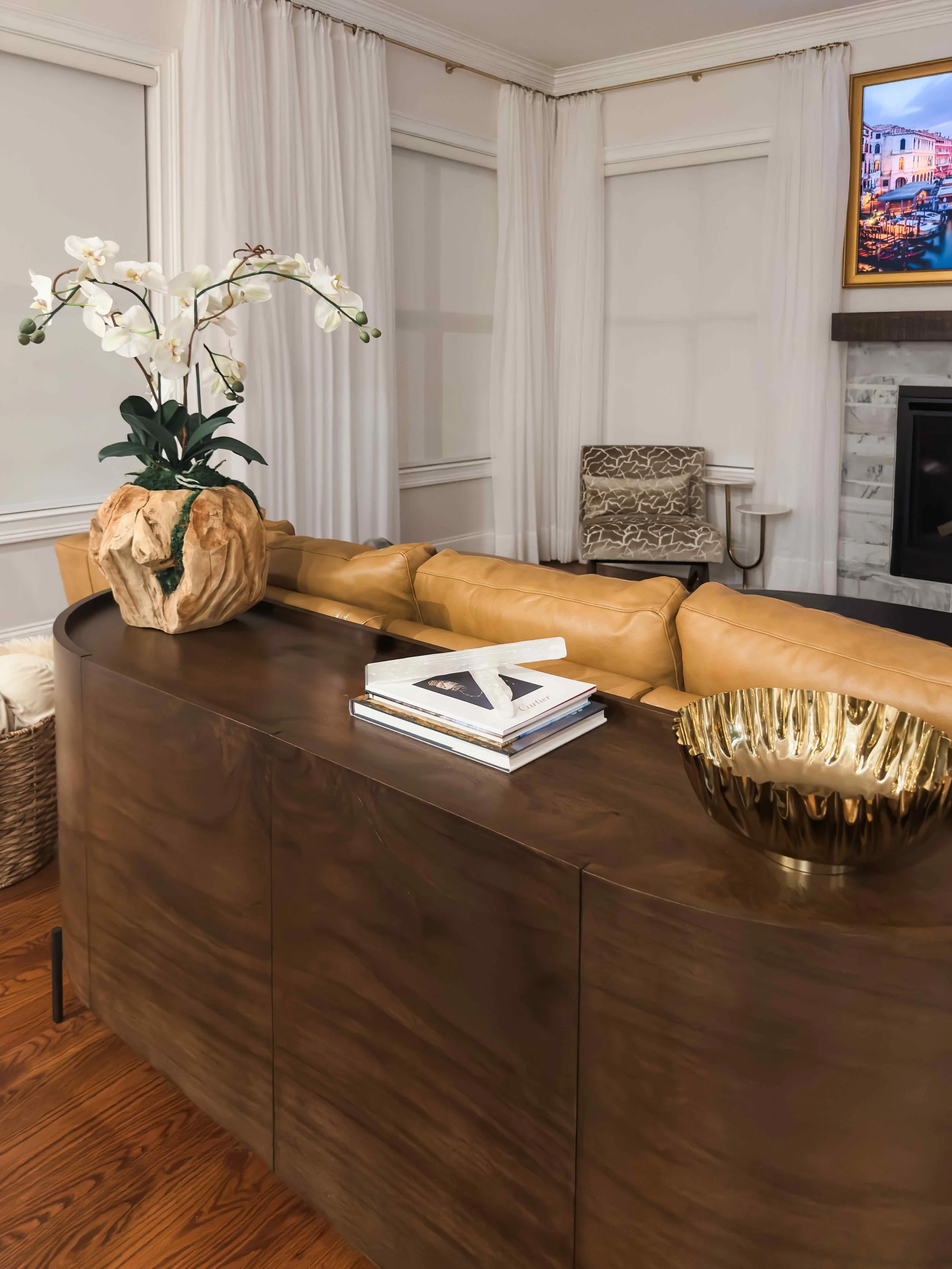 Noble family room in East Cobb with a curved walnut sofa table, camel leather sectional, orchid arrangement, and stone fireplace, designed by Luxe Style Studio