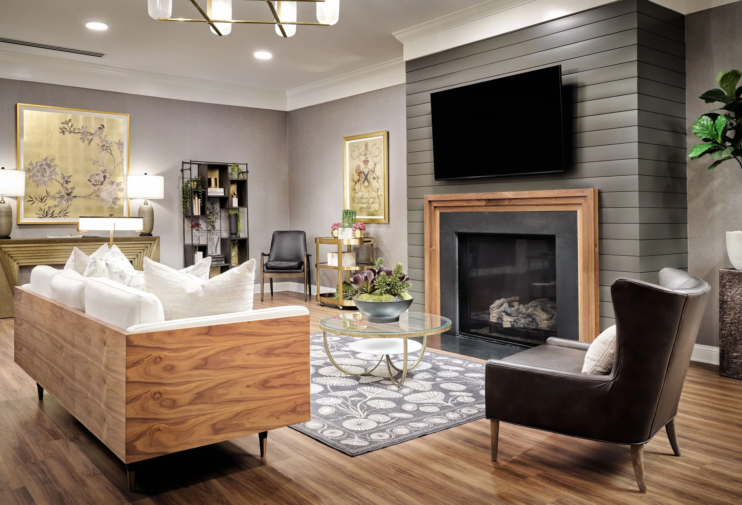 Lounge with walnut-backed white sofa, dark shiplap fireplace surround, chinoiserie gold artwork, and leather wing chair, Finn & Fox lounge, Sugar Hill, GA, interior design by Ashley Schneider