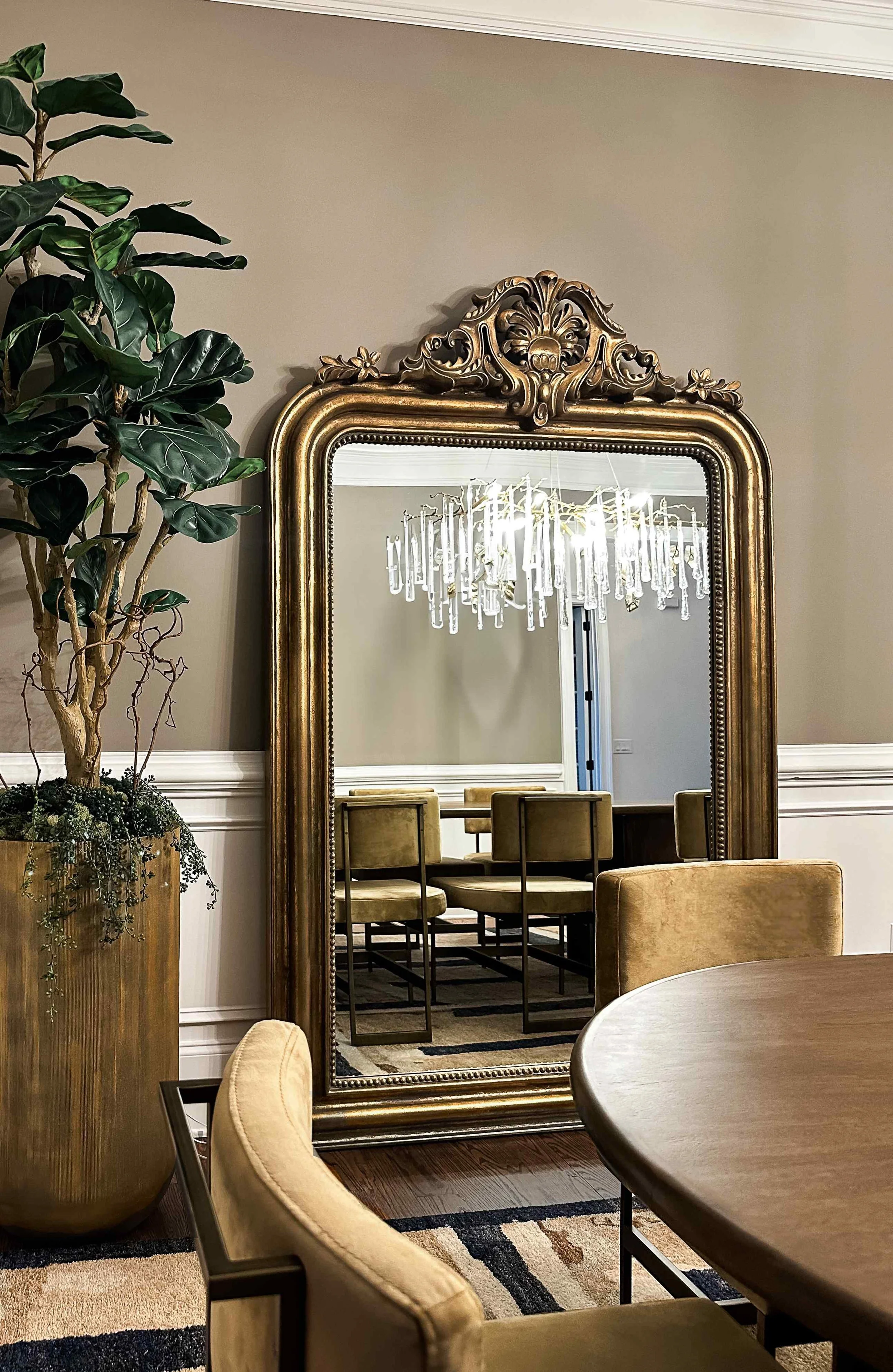 Noble dining room in East Cobb with an ornate gold mirror, olive velvet dining chairs, a round wood table, and a fiddle-leaf fig, designed by Luxe Style Studio