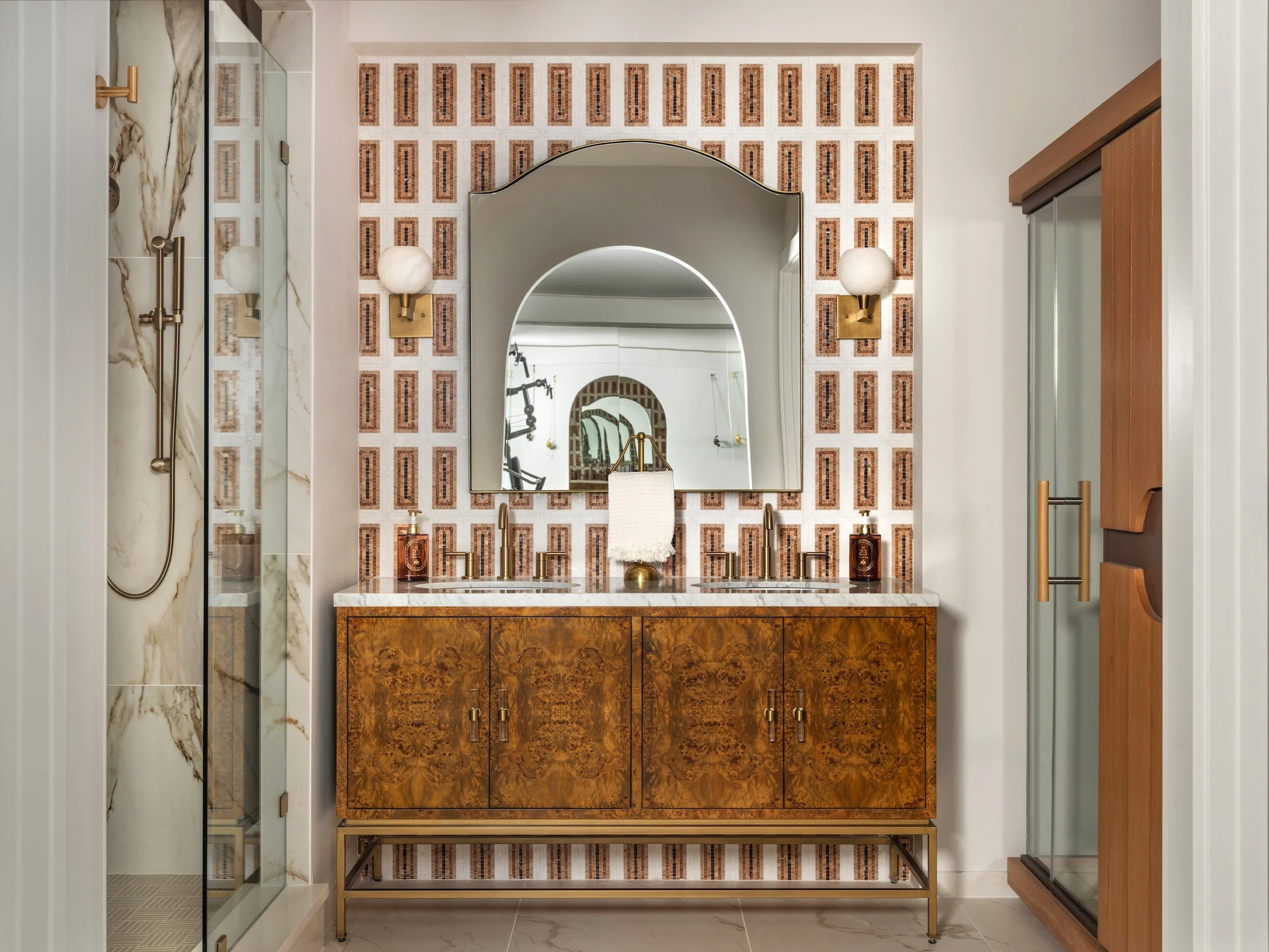 Gym bath with burl-wood vanity, geometric tile, brass sconces, and infrared sauna, designed by Luxe Style Studio