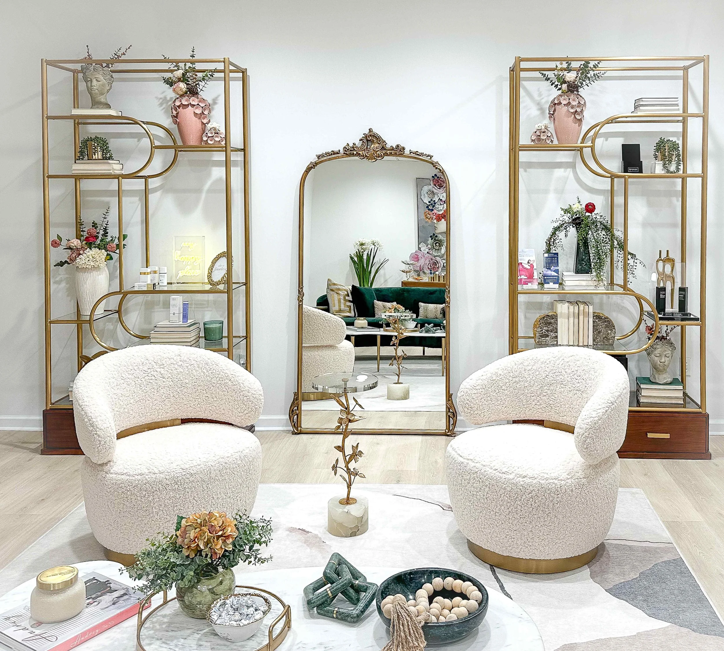 Luxury medical spa waiting room with cream bouclé swivel chairs, paired gold art deco etageres styled with botanicals and sculptures, and ornate gold floor mirror, interior design by Luxe Style Studio