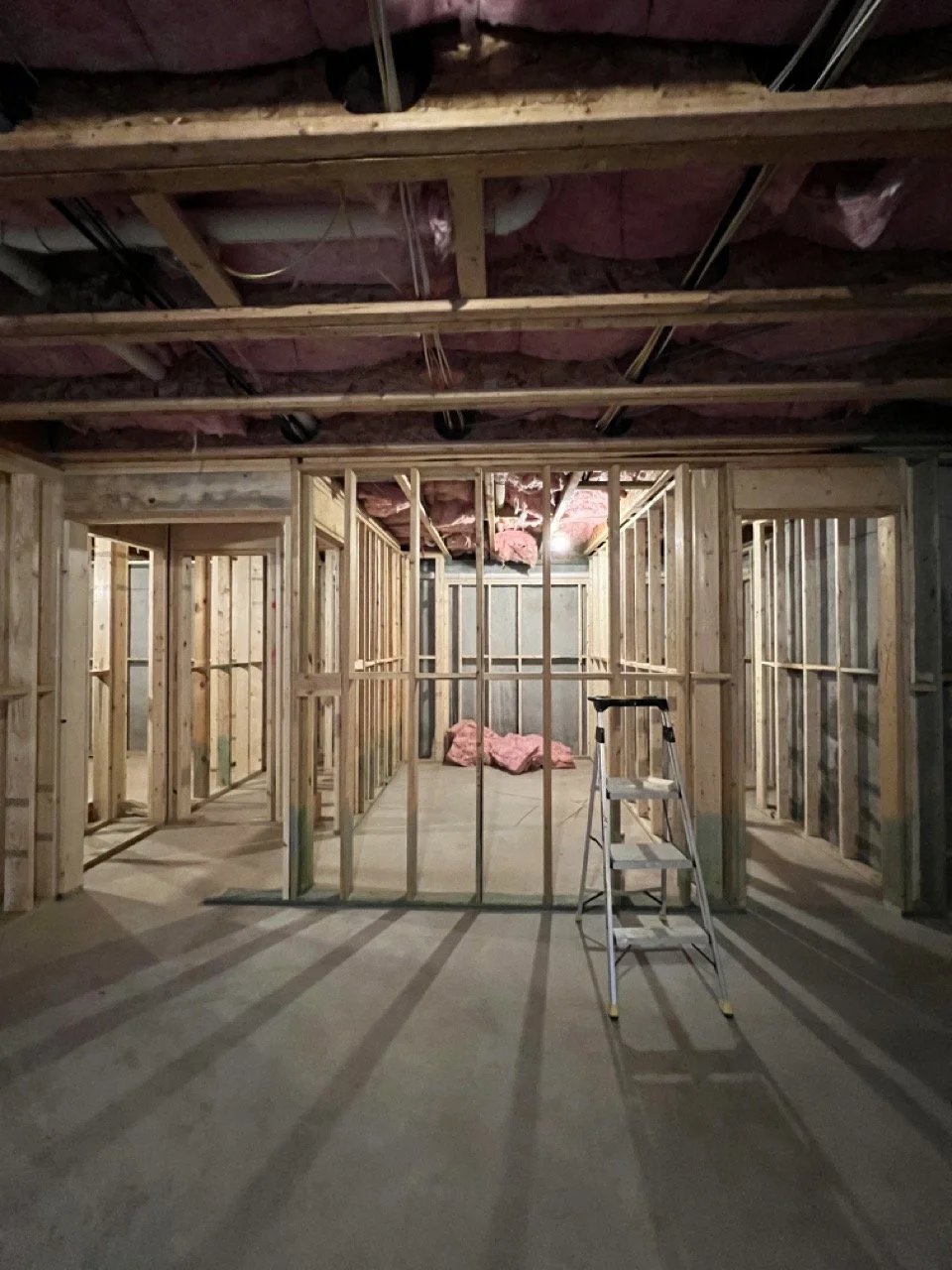 Framing stage of a whole-home renovation with exposed wall studs, ceiling insulation, and construction ladder