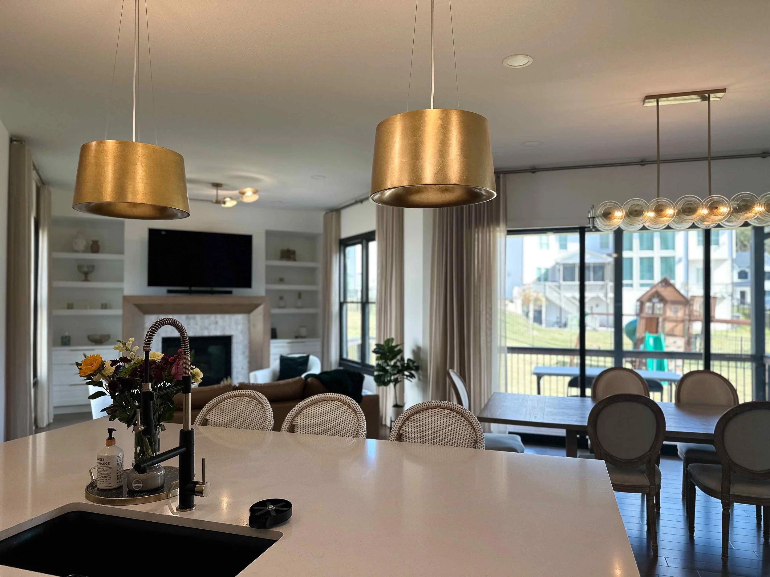 Open-concept kitchen and dining space with gold drum pendants, glass globe linear chandelier, and view to great room by Luxe Style Studio