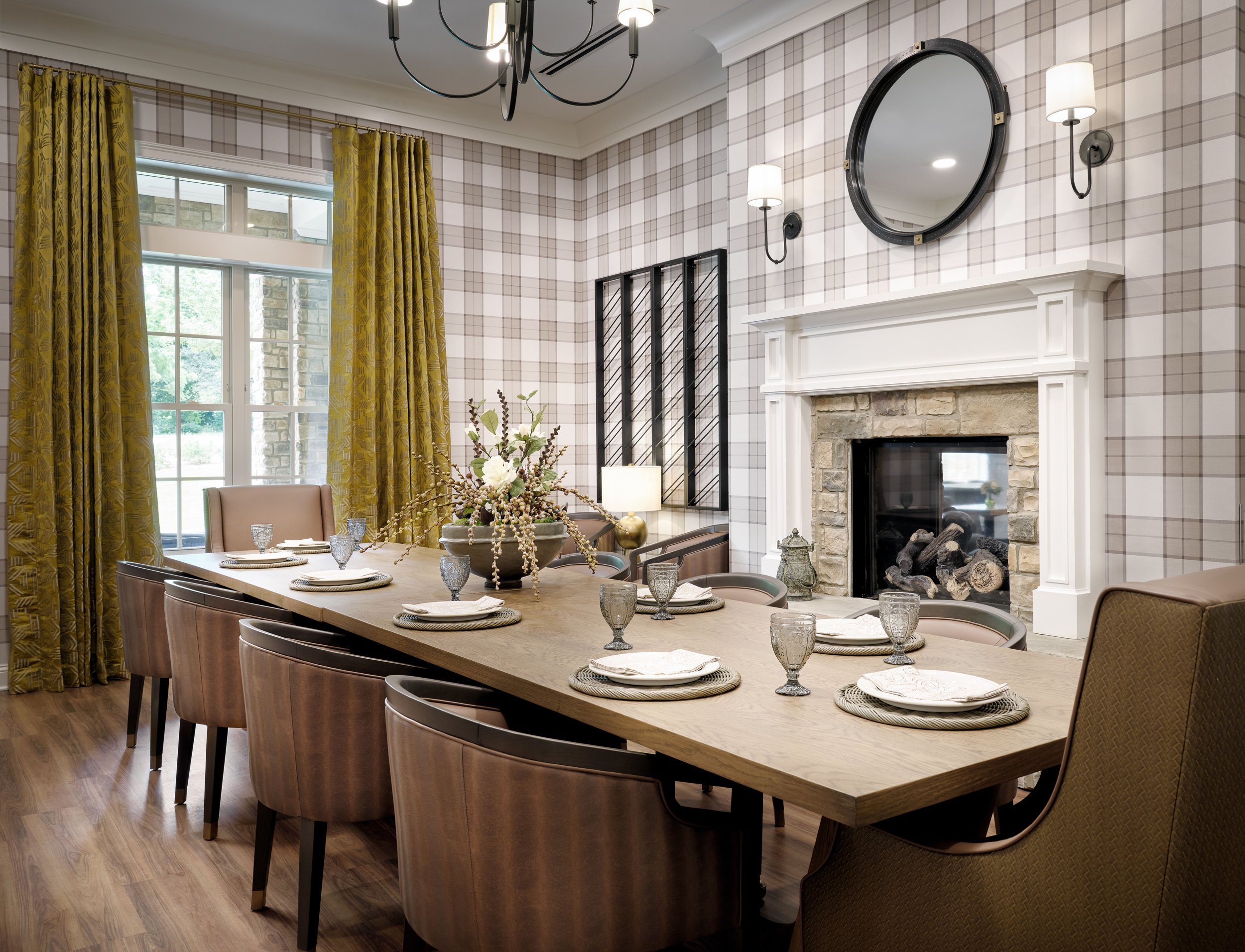 Private dining room with plaid wallpaper, stone fireplace, olive gold drapery, set dining table, and porthole mirror, Thistle & Oak restaurant, Sugar Hill, GA, interior design by Ashley Schneider