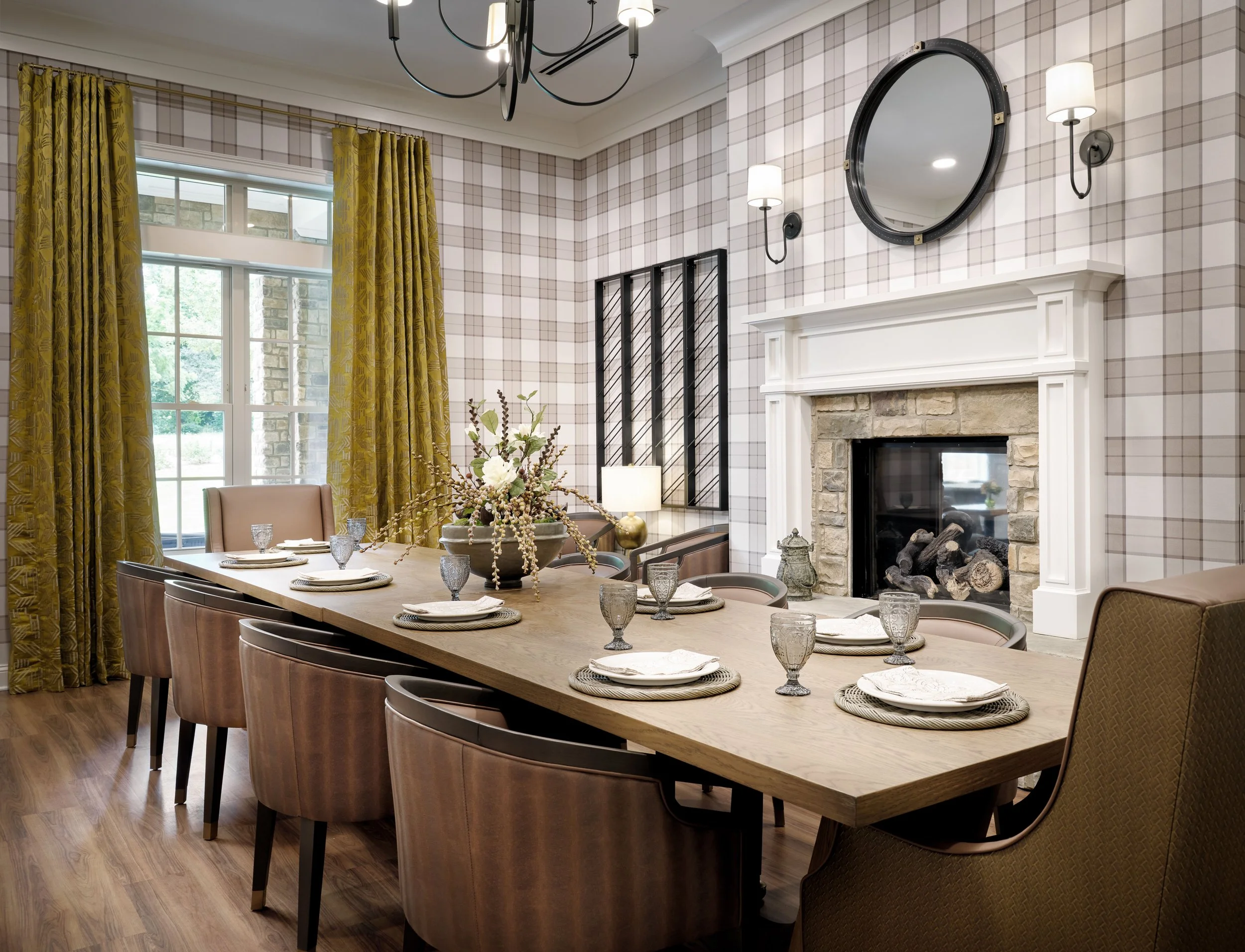 Private dining room with plaid wallpaper, stone fireplace, olive gold drapery, set dining table, and porthole mirror, Finn & Fox lounge, Sugar Hill, GA, interior design by Ashley Schneider