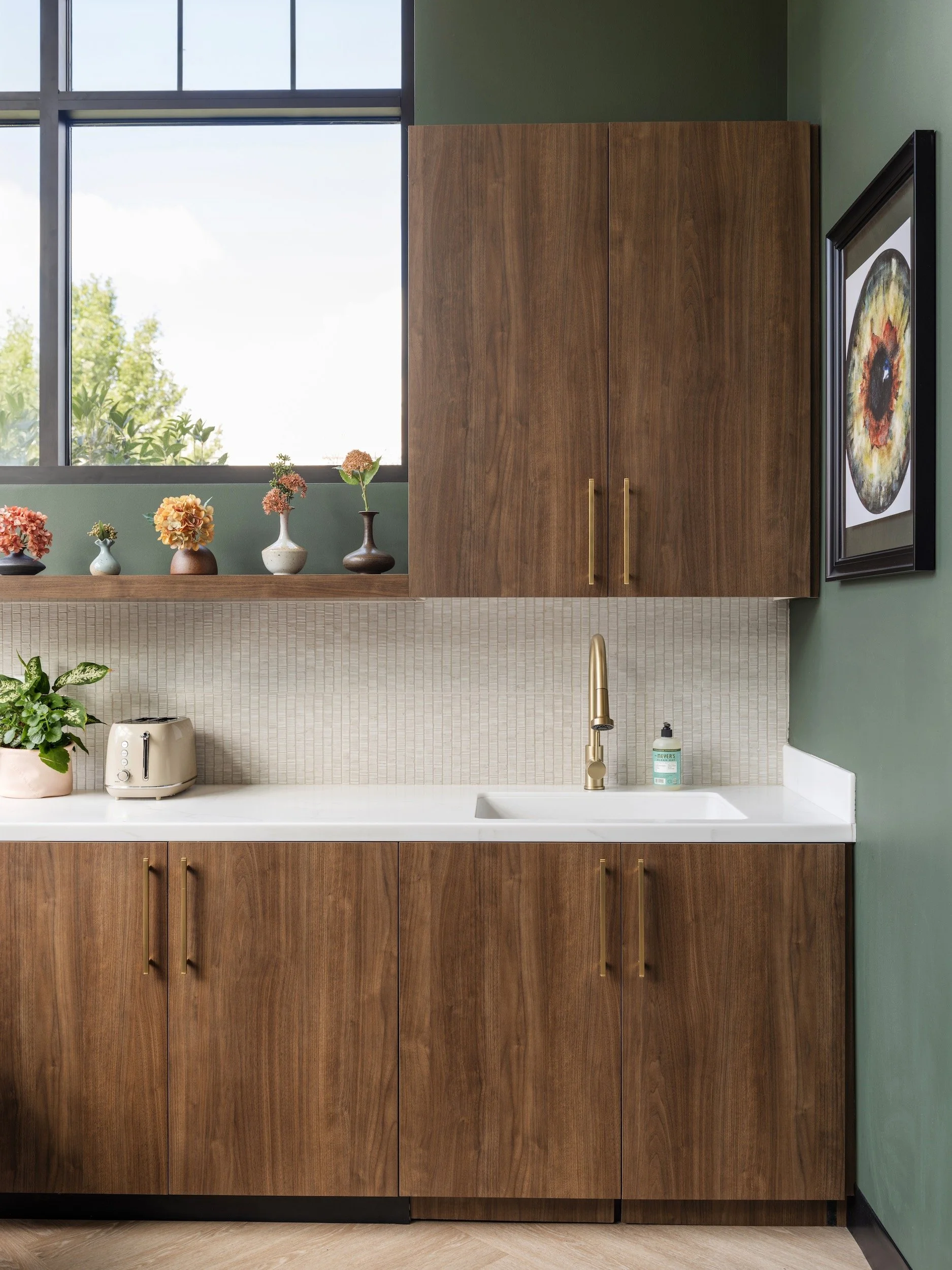 Walnut staff kitchen cabinetry with brass hardware, white mosaic tile, and forest green walls, designed by Luxe Style Studio