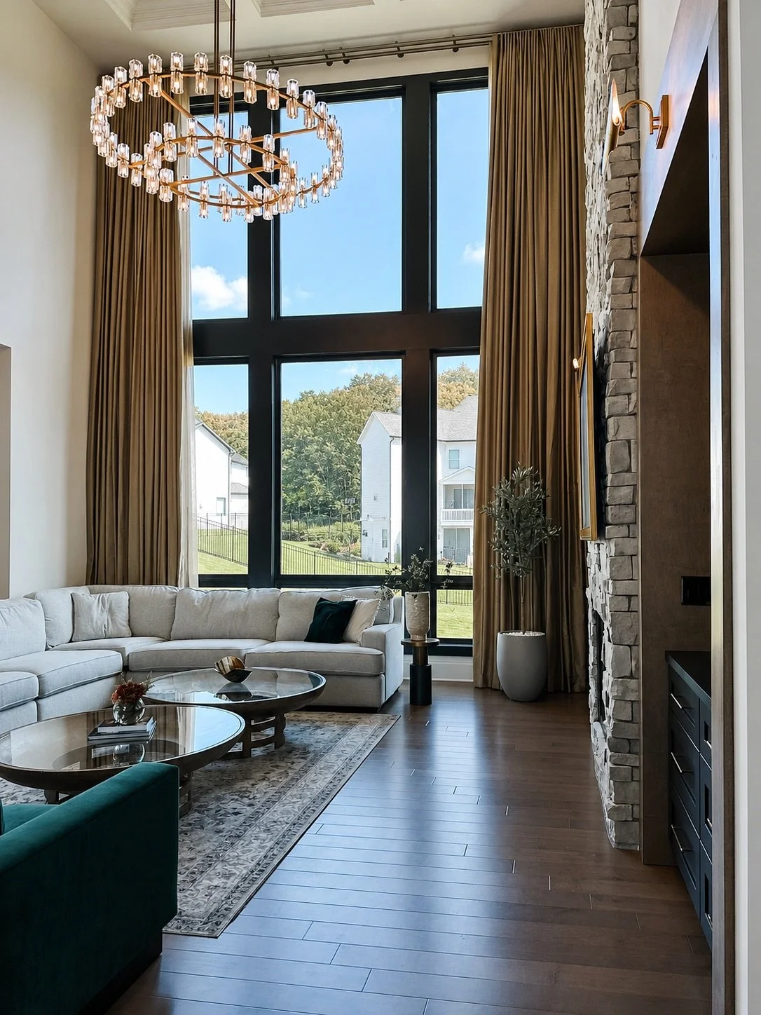 Two-story East Cobb great room with a crystal ring chandelier, floor-to-ceiling bronze drapery, tall black-framed windows, and a sectional, designed by Luxe Style Studio