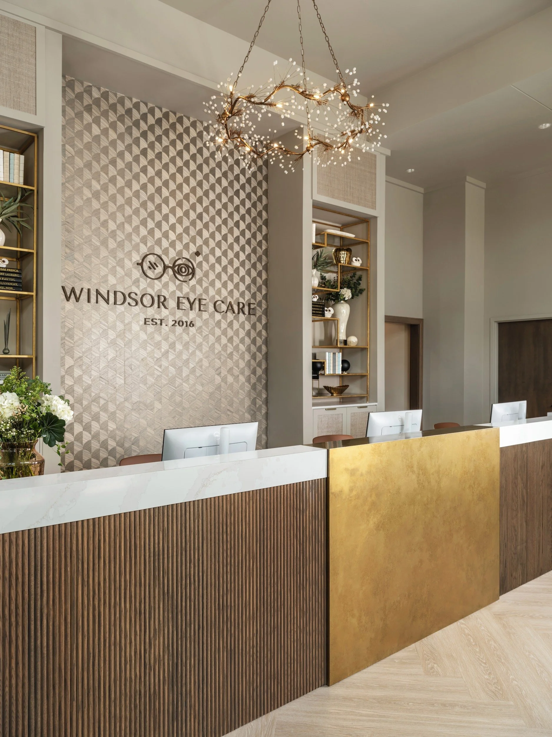Boutique medical office reception area with sculptural branch chandelier, gold leaf desk panel, fluted walnut millwork, and herringbone white oak floors, Windsor Eye Care optical boutique, Atlanta, GA, interior design by Luxe Style Studio
