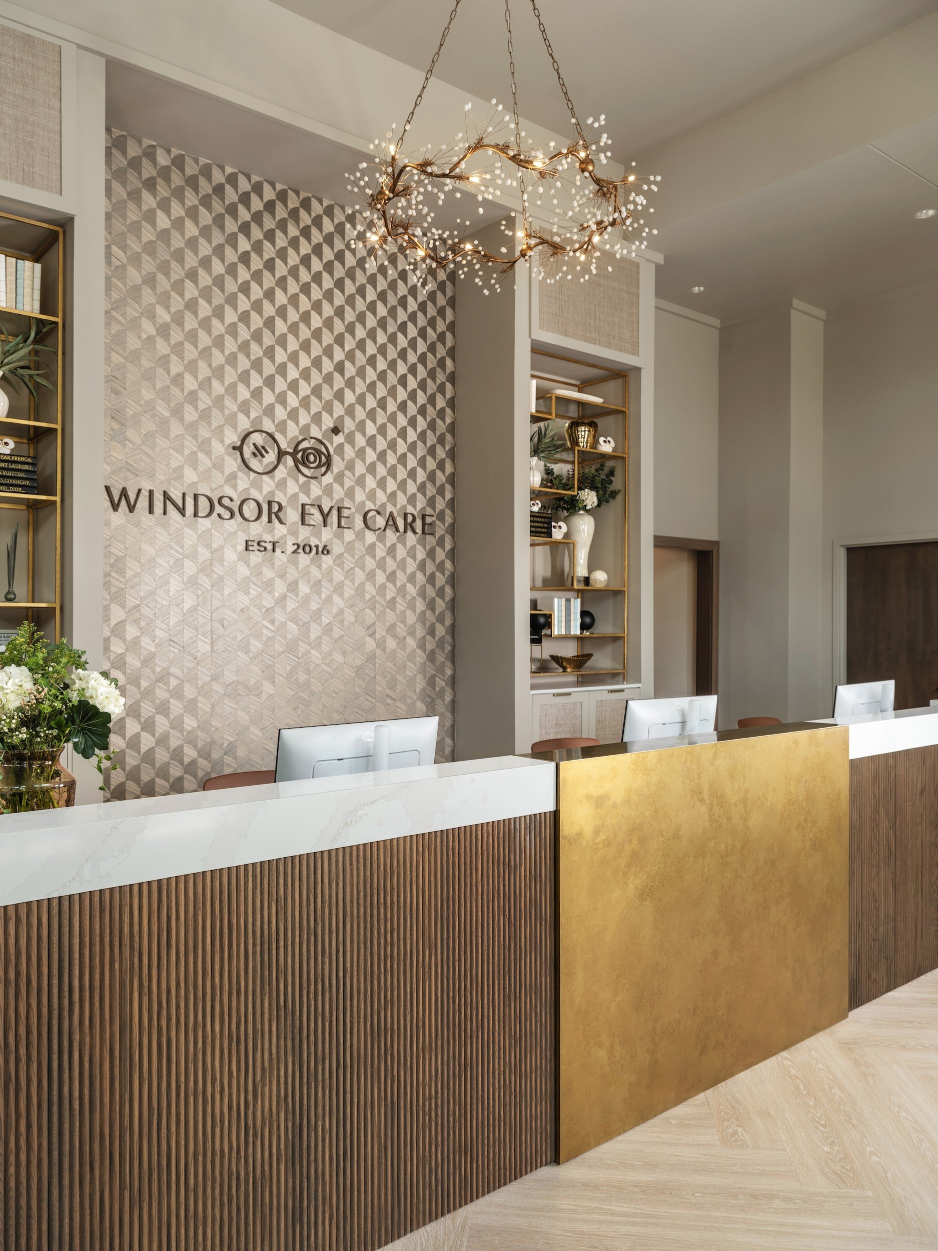 Windsor Eye Care reception area with a branch chandelier, custom eyewear displays, and herringbone floors, designed by Luxe Style Studio