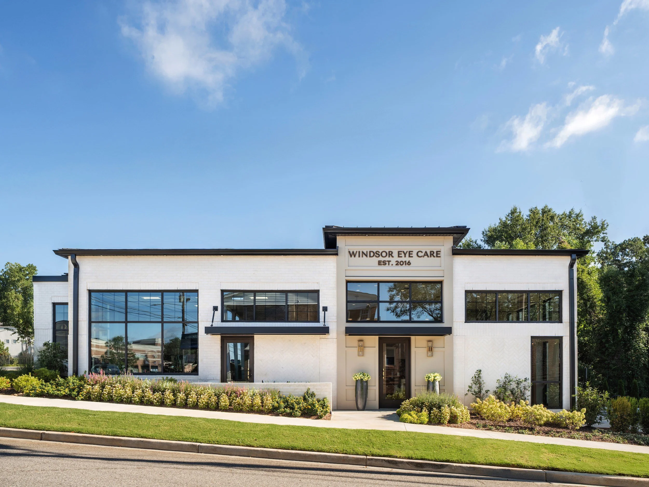 Rustic white painted brick commercial building exterior with black steel windows and lush landscaping, Windsor Eye Care optical boutique, Atlanta, GA, interior design by Luxe Style Studio