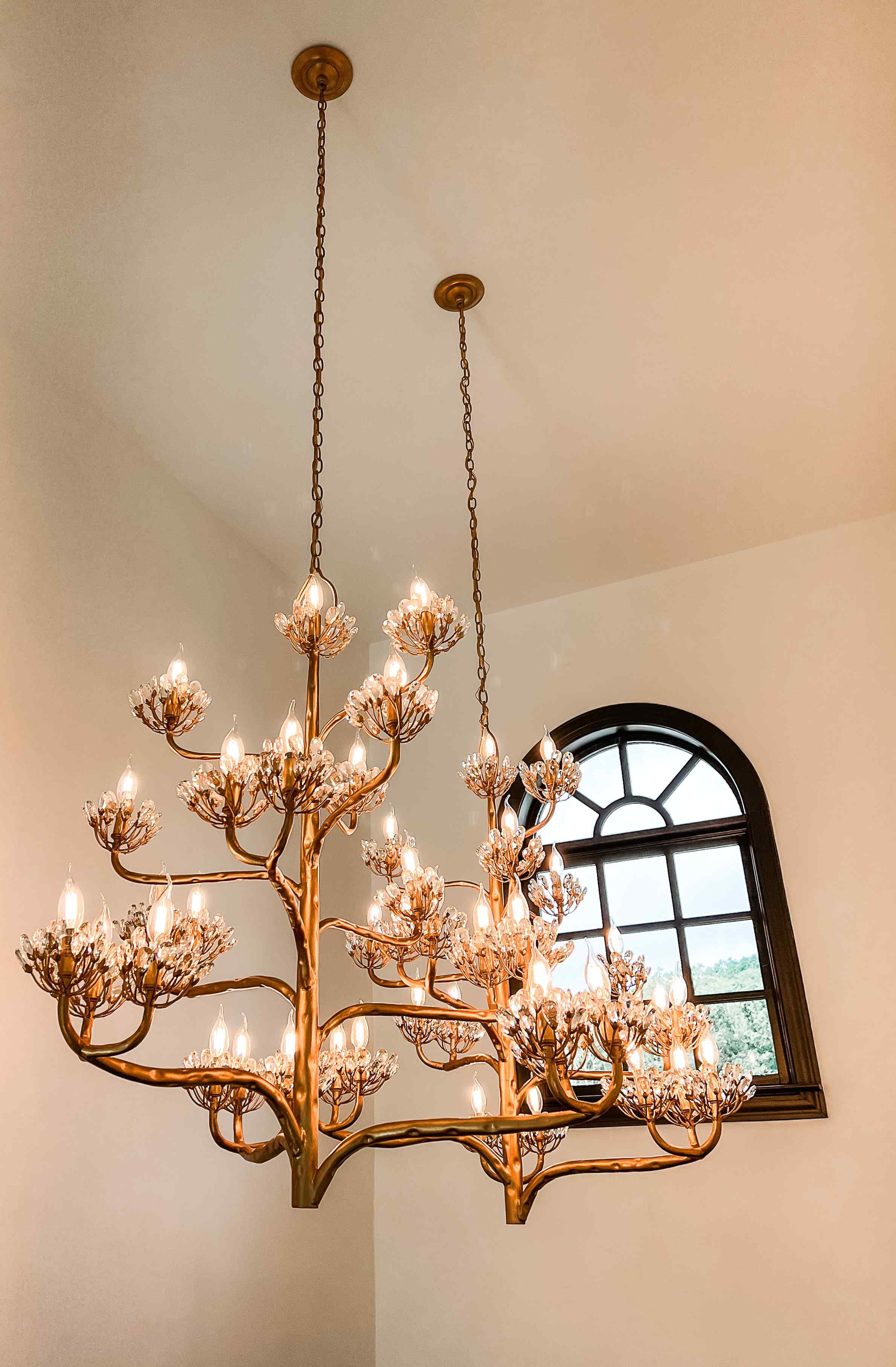 Statement brass tree-branch chandelier with crystal floral clusters illuminating a foyer with arched window, Luxe Style Studio