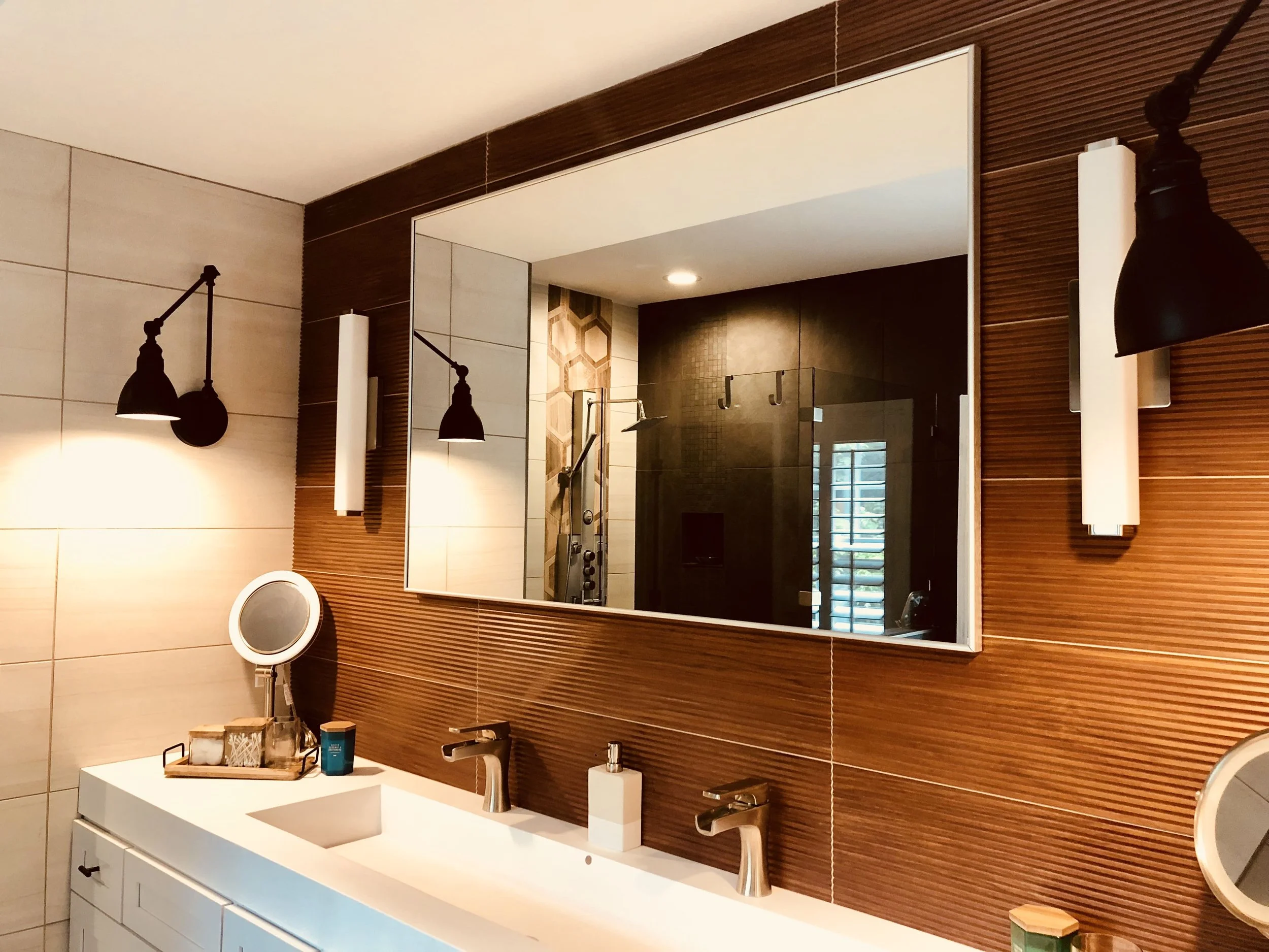 Buckhead primary bathroom double vanity with textured wood-look tile accent wall, matte black swing-arm sconces, and large frameless mirror by Luxe Style Studio