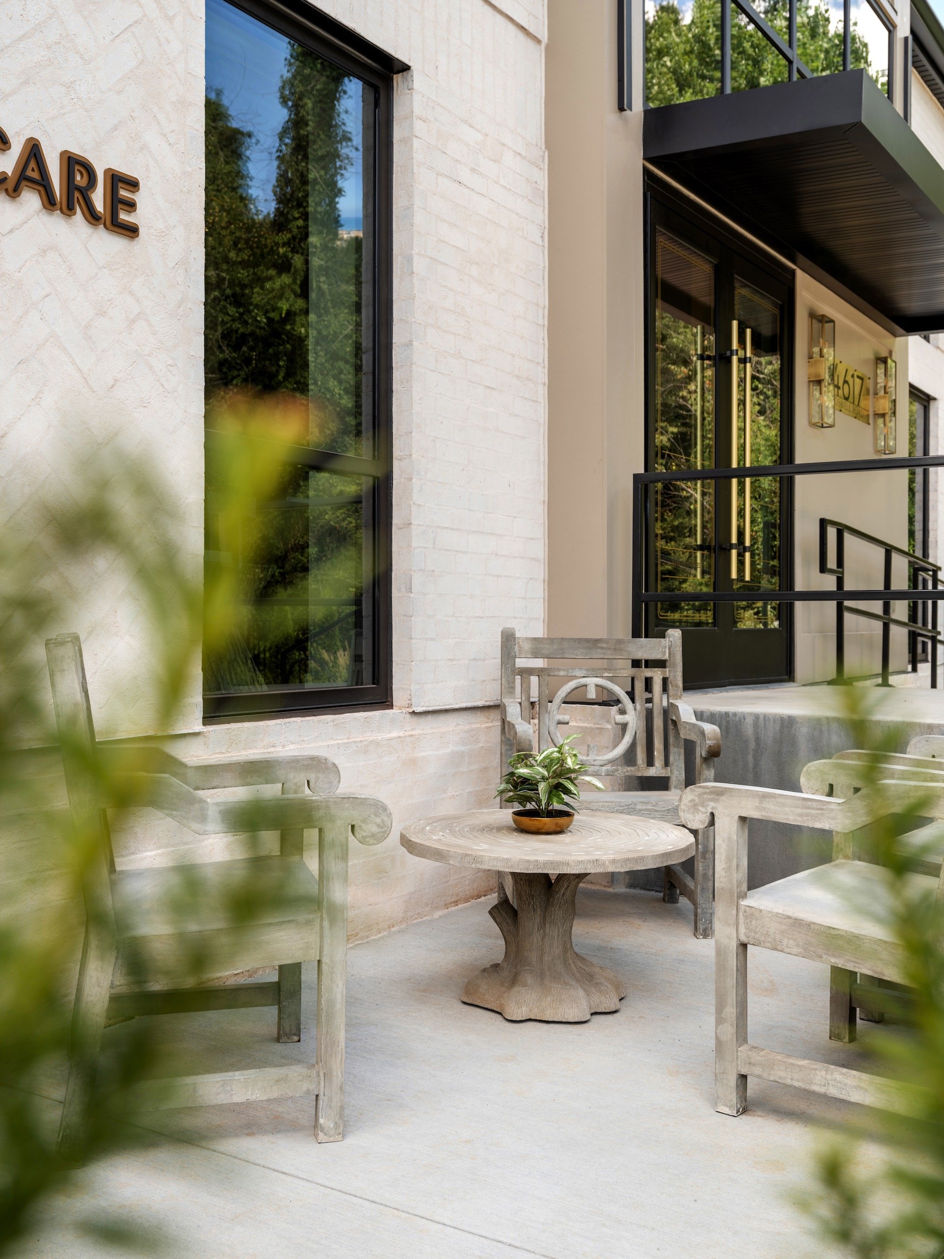Boutique commercial outdoor seating area with weathered stone armchairs and pedestal table beside white brick exterior, Windsor Eye Care optical boutique, Atlanta, GA, interior design by Luxe Style Studio