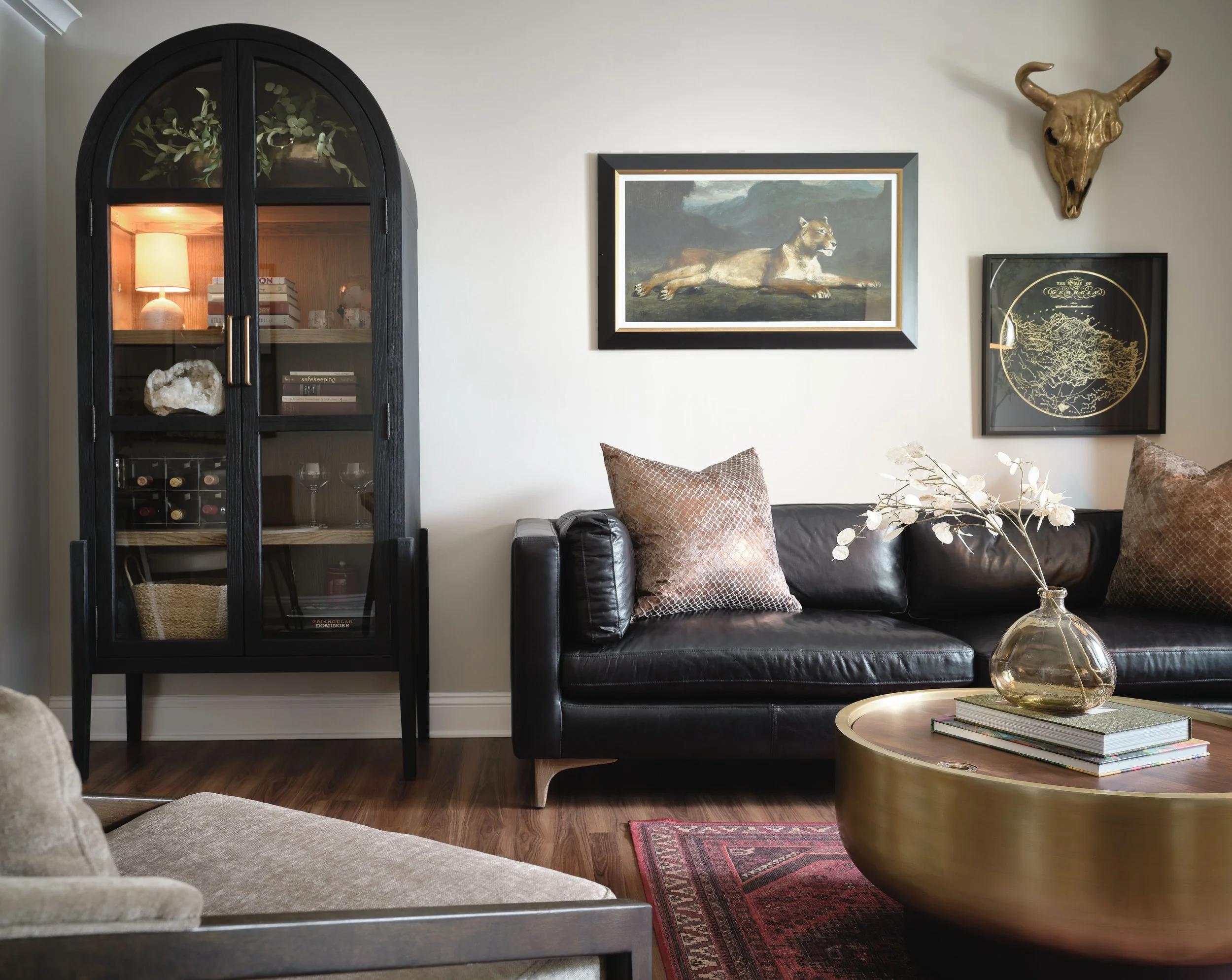 Living room with black arched glass display cabinet, brass drum coffee table, vintage Persian rug, and animal art gallery wall, Sugar Hill, GA private residence, interior design by Ashley Schneider