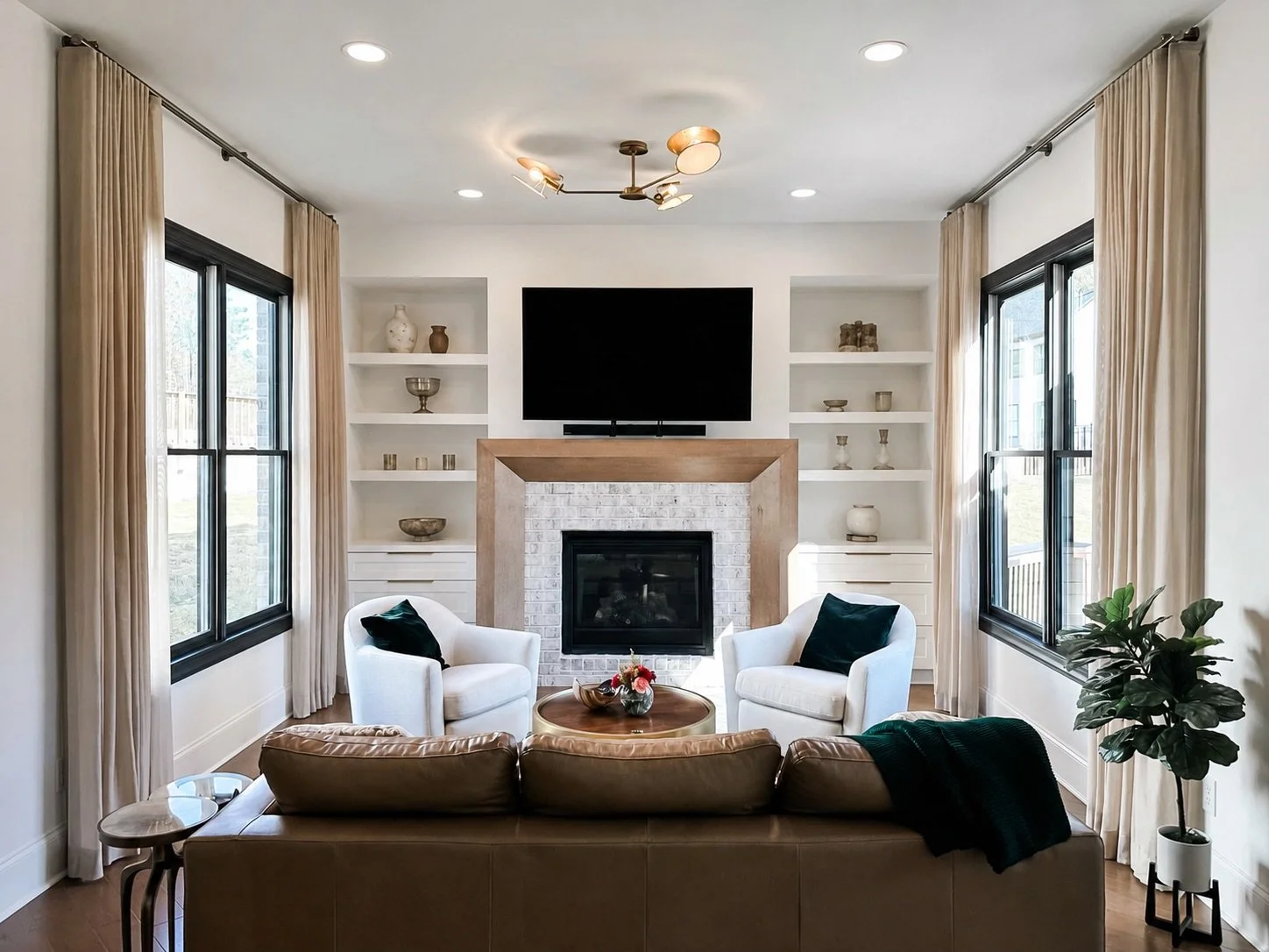 East Cobb living room with a leather sofa, white accent chairs, fireplace, styled built-in shelving, and tailored neutral drapery, designed by Luxe Style Studio